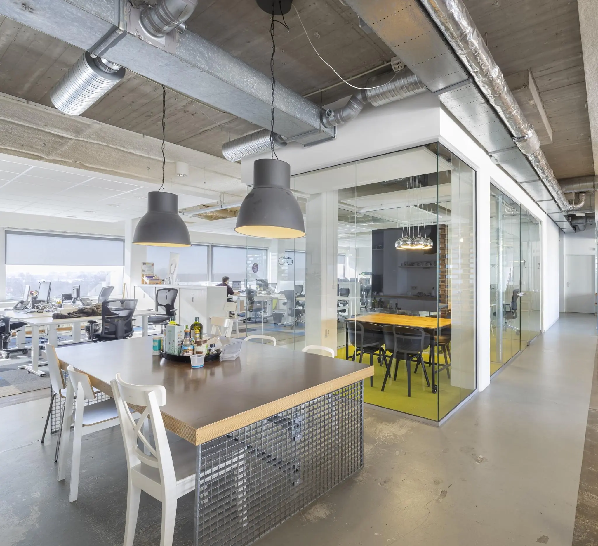 Modern kantoorinterieur aan de Joan Muyskenweg met open werkplekken, glazen vergaderruimte en een gemeenschappelijke tafel.