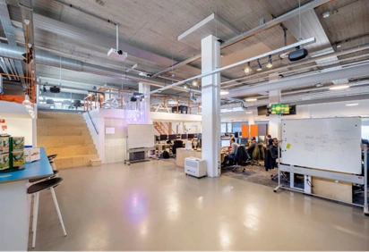 Modern kantoorinterieur aan de Joan Muyskenweg met werkplekken, whiteboard en trap naar een vide.