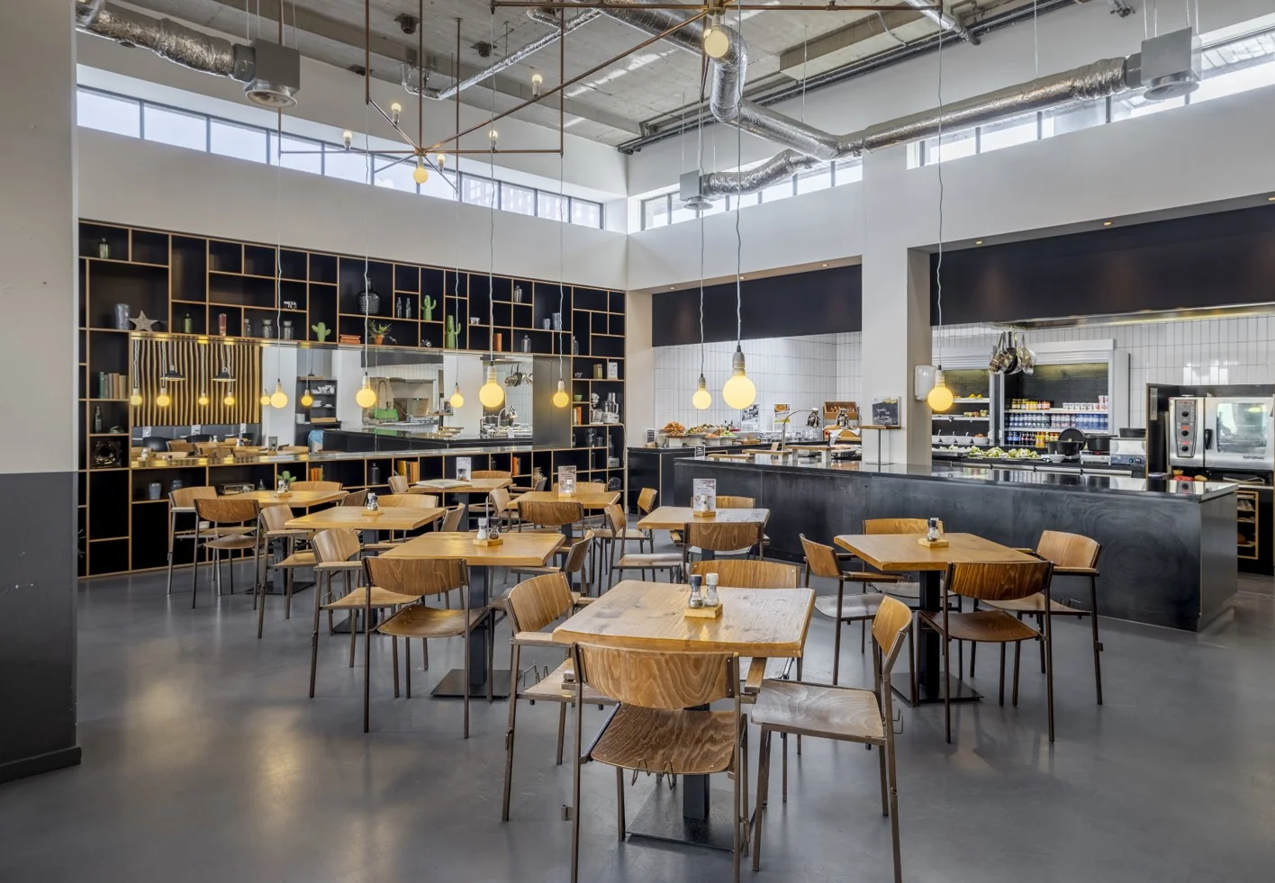 Modern ingerichte bedrijfsrestaurant aan de Joan Muyskenweg met houten meubilair, open keuken en industriële details.