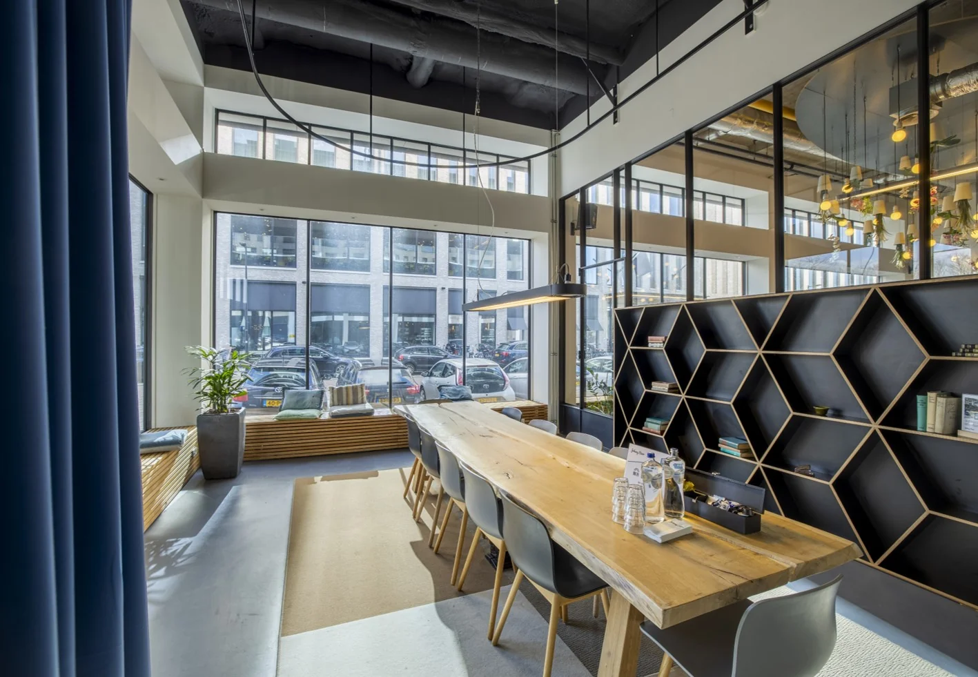 Moderne vergaderruimte aan de Joan Muyskenweg met een lange houten tafel, design boekenwand en grote ramen met uitzicht op geparkeerde auto's.