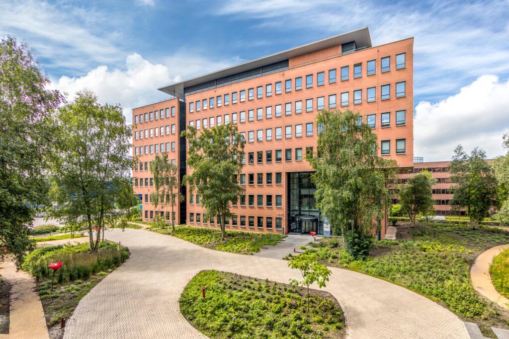Modern kantoorgebouw aan de Hullenbergweg omgeven door groen en een betegeld pad.
