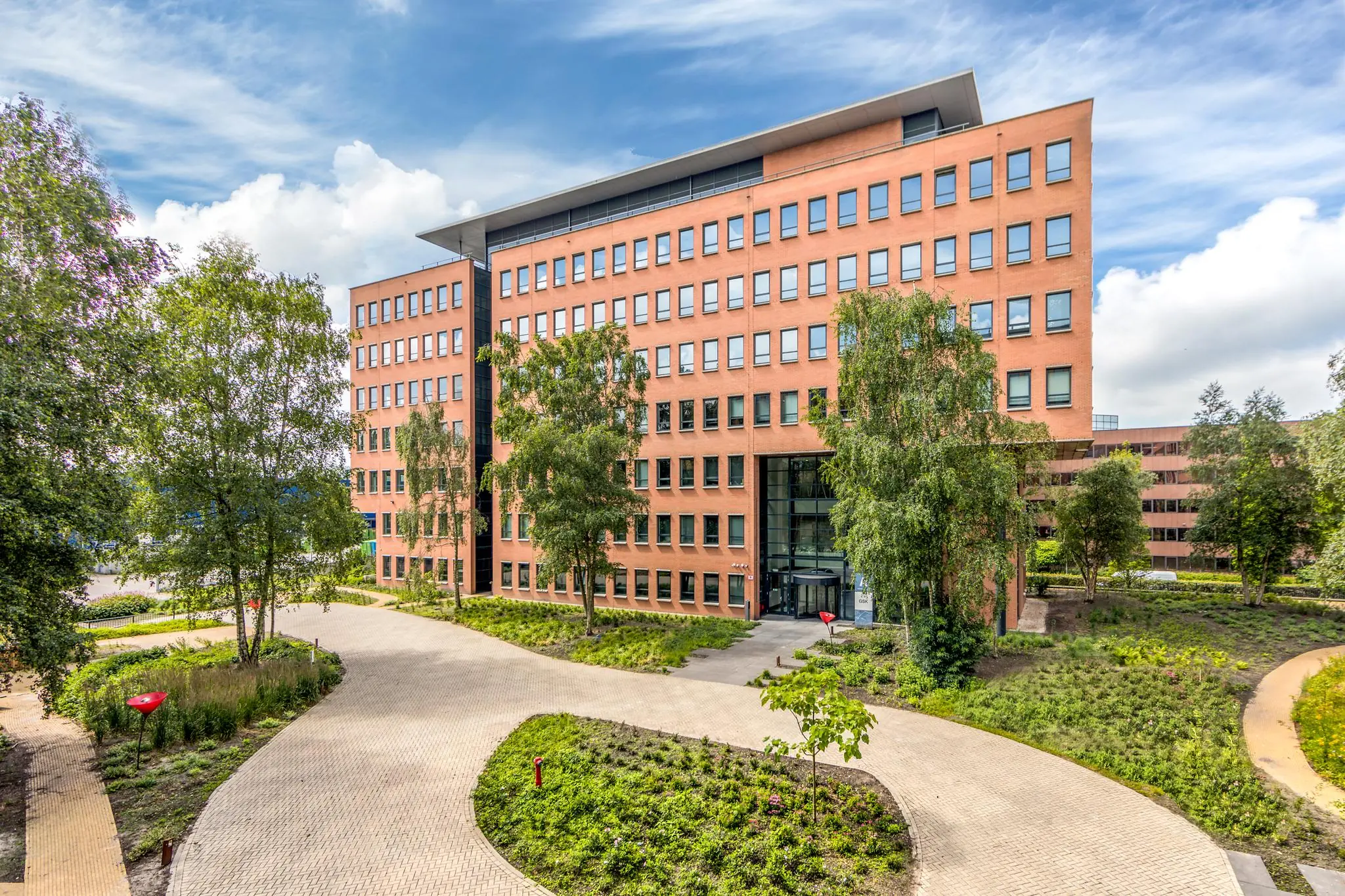 Modern kantoorgebouw aan de Hullenbergweg omgeven door groen en een betegeld pad.