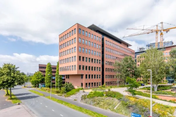 Kantoorgebouw aan de Hullenbergweg in Amsterdam-Zuidoost met omliggende groenvoorziening en bouwkranen op de achtergrond.