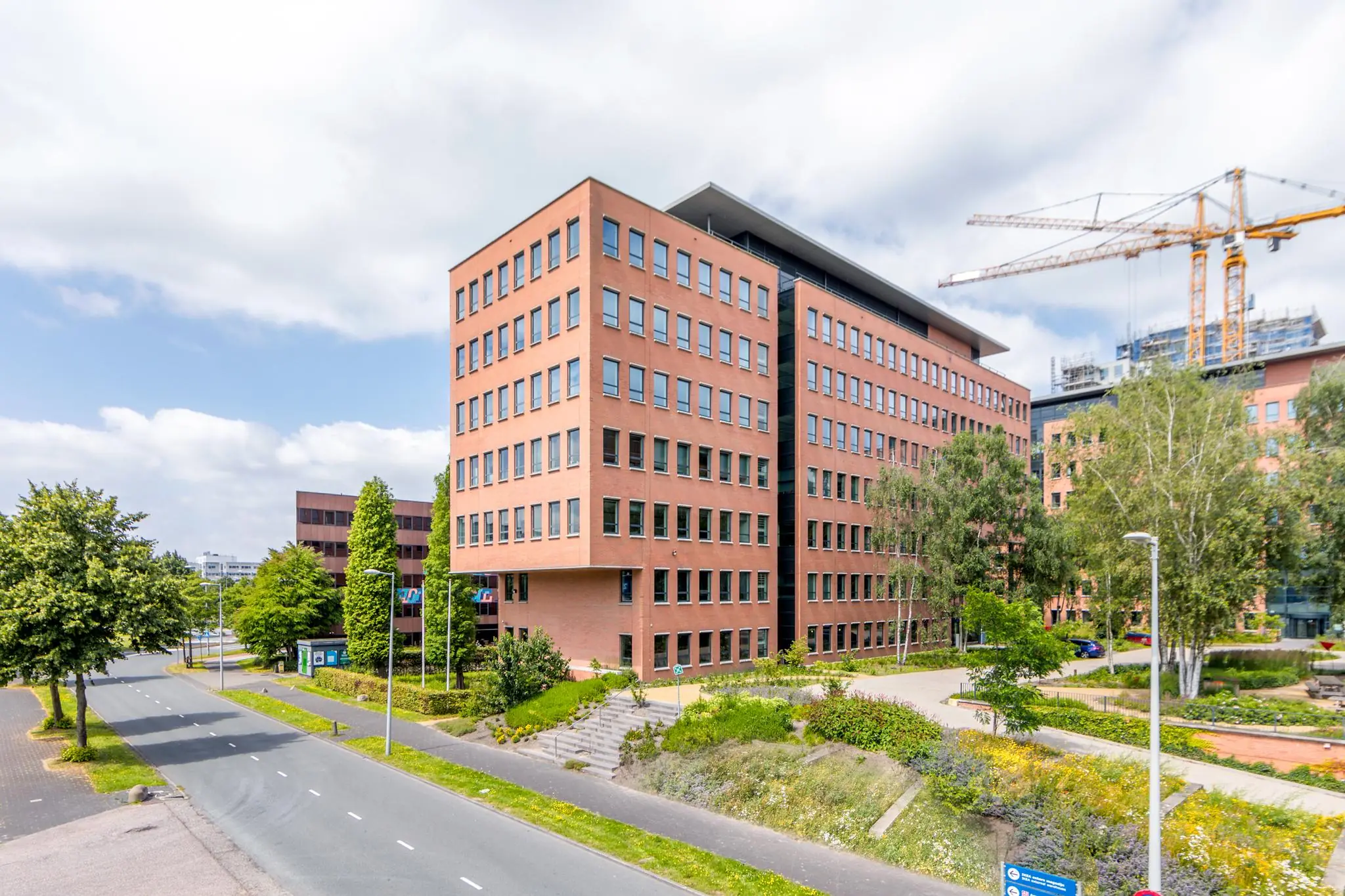Kantoorgebouw aan de Hullenbergweg in Amsterdam-Zuidoost met omliggende groenvoorziening en bouwkranen op de achtergrond.