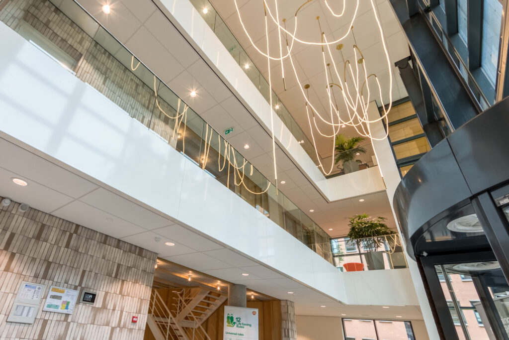 Moderne entreehal van een kantoorpand aan de Hullenbergweg met glazen balustrades, opvallende lichtinstallatie en open trappenhuis.