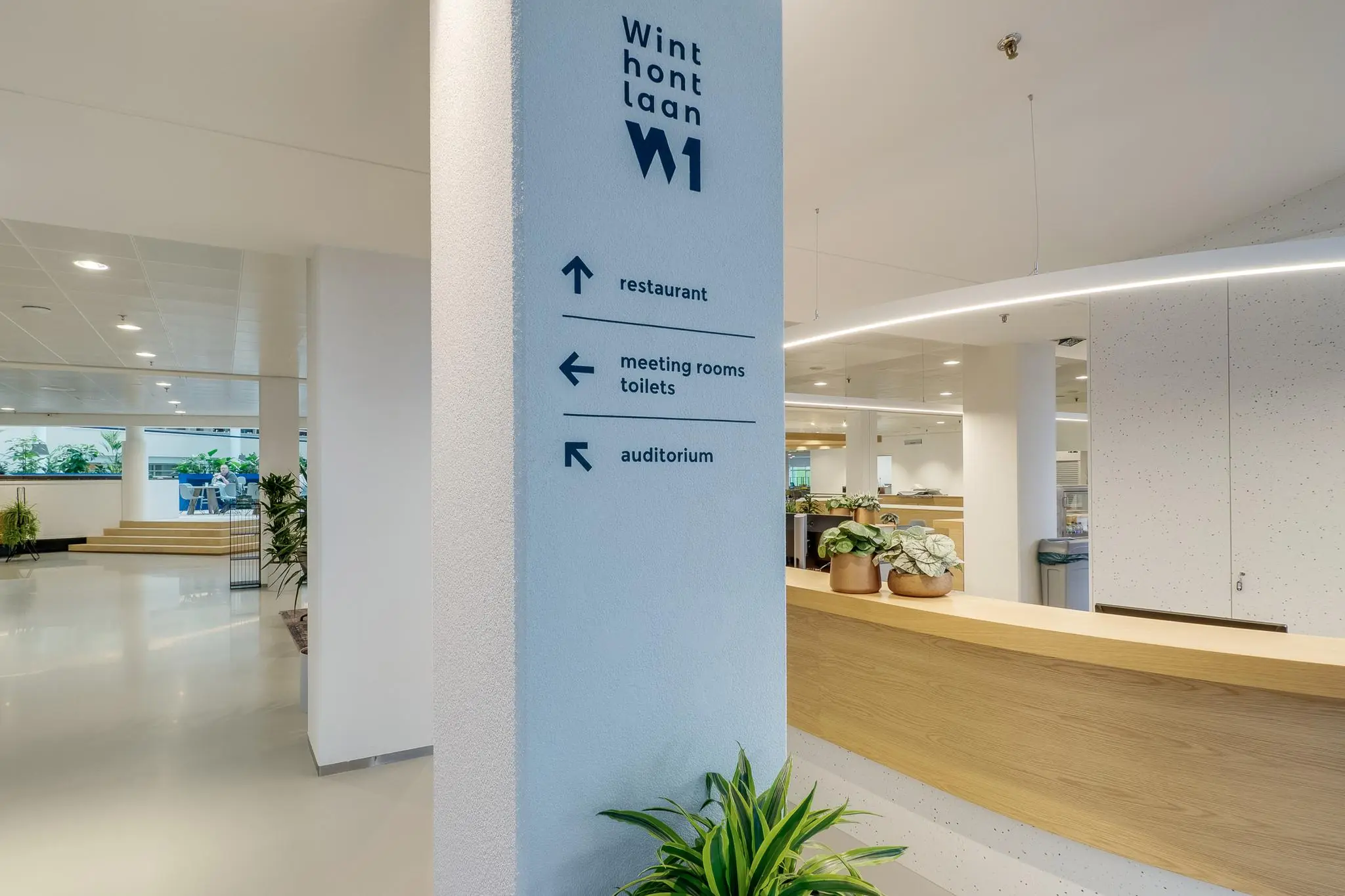 Moderne, lichte ontvangsthal in het Winthontlaan W1-gebouw met bewegwijzering naar restaurant, vergaderruimtes, toiletten en auditorium.