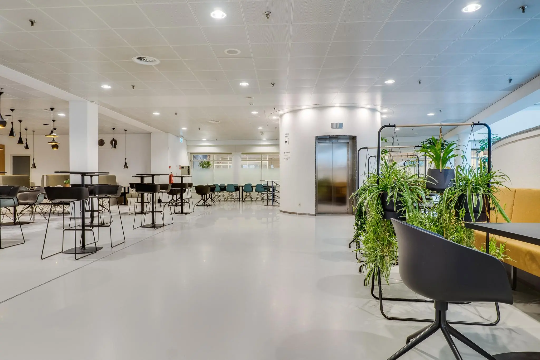 Moderne en ruimtelijke kantoorlounge aan de Winthontlaan met zitgelegenheden, hangplanten en een lift in het midden.