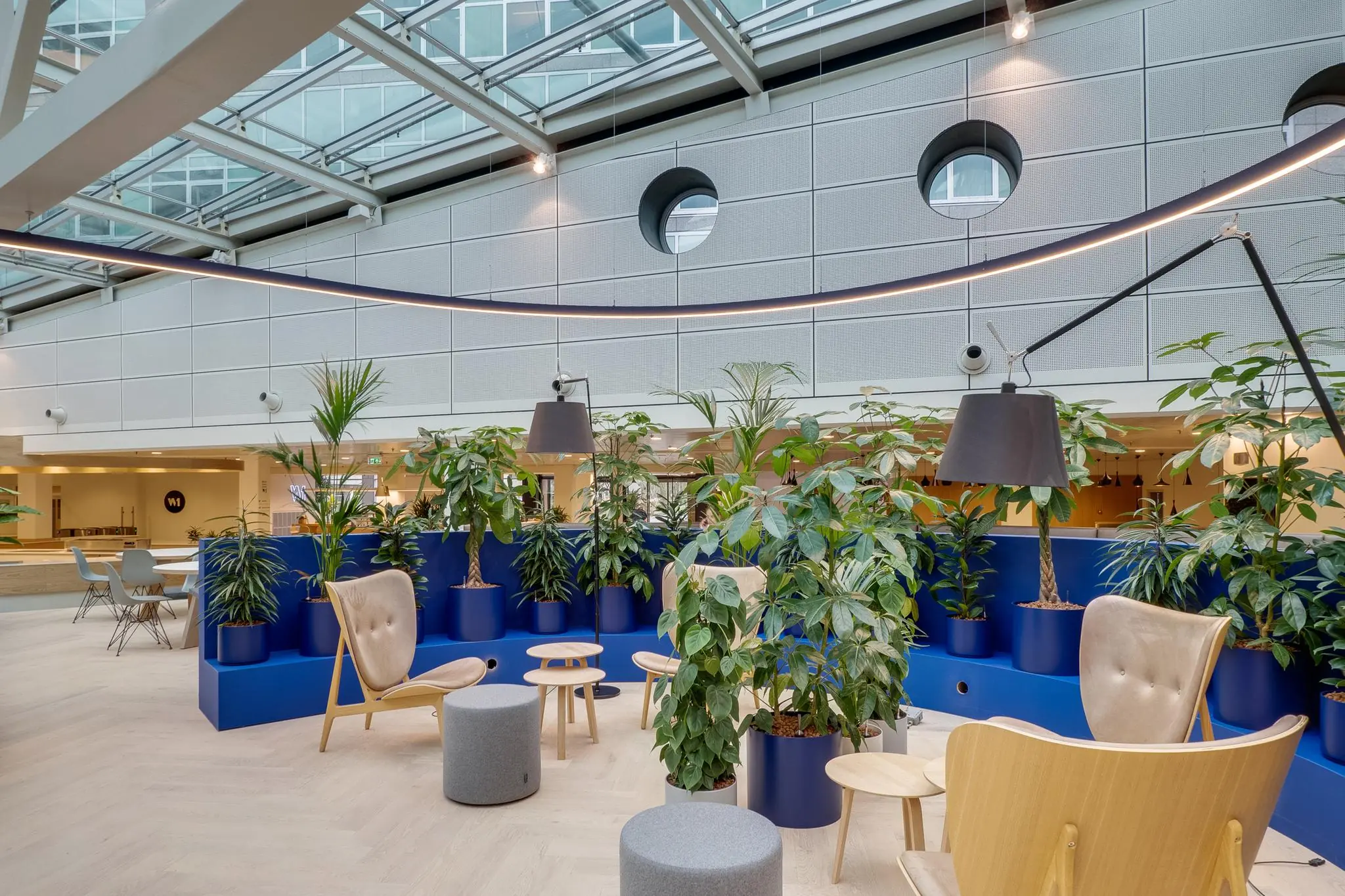 Moderne, lichte zithoek op de Winthontlaan met houten meubels, planten in blauwe potten en een glazen dak.