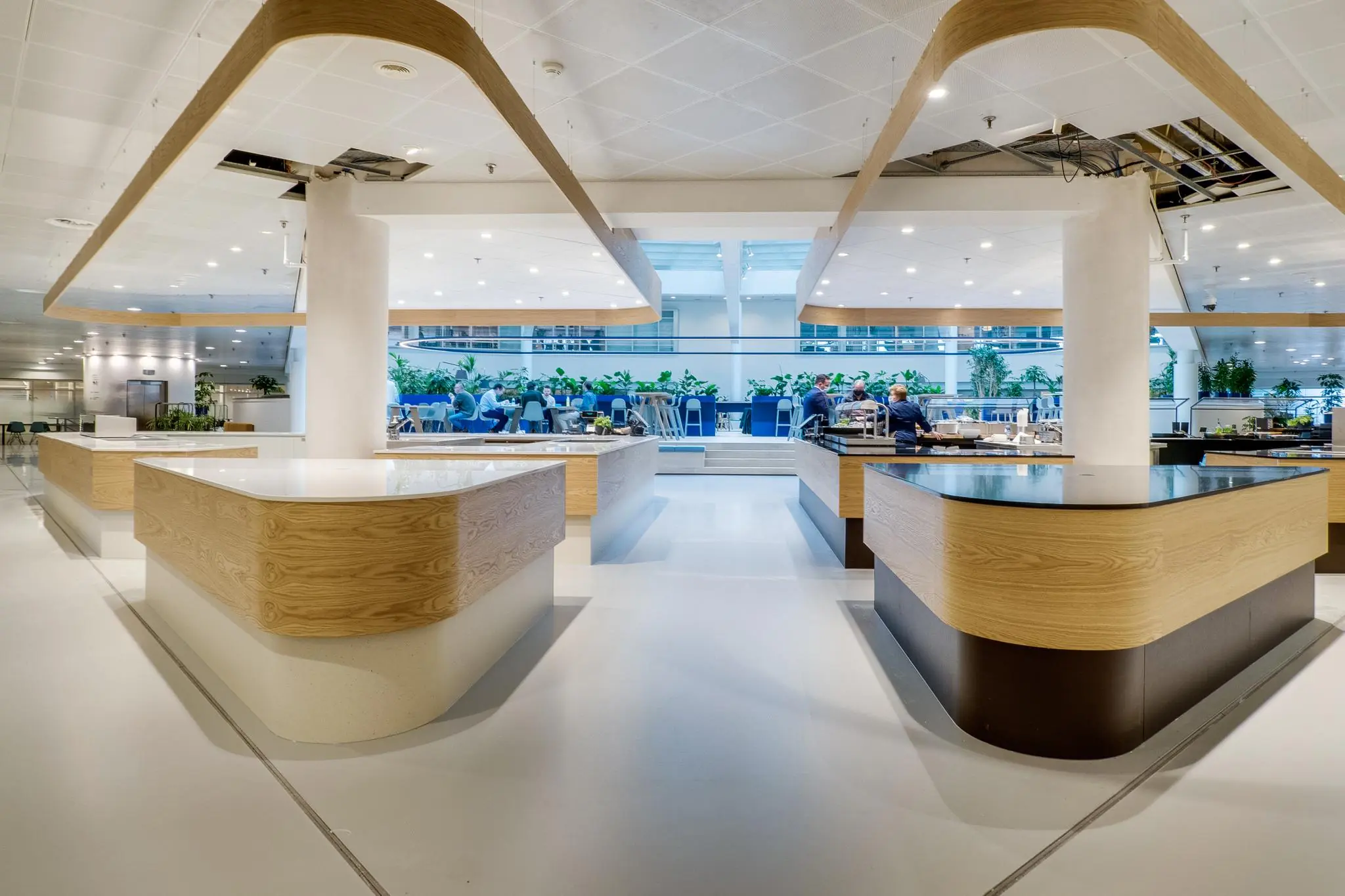 Modern bedrijfsrestaurant aan de Winthontlaan met houten serveereilanden en een open zithoek met veel planten.