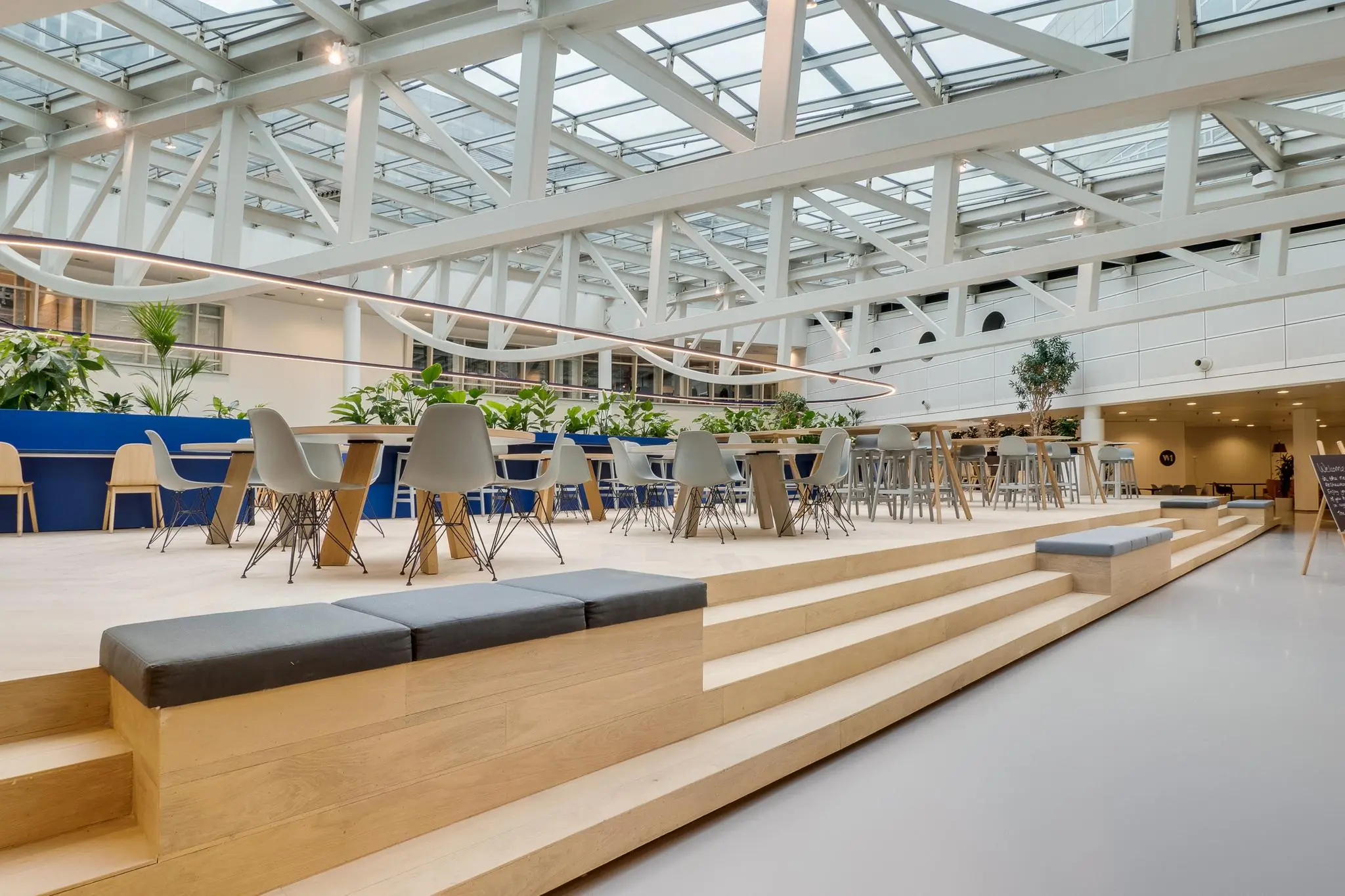 Moderne, open kantoorruimte aan de Winthontlaan met houten zittribune, planten en designmeubilair onder een glazen dak.