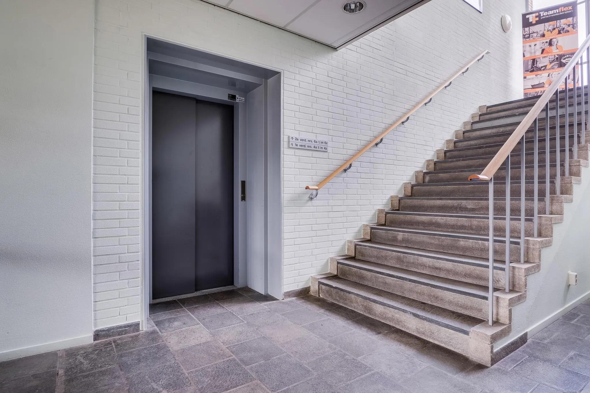 Moderne entree met een grijze liftdeur en een trap met houten leuning bij Kernkade.