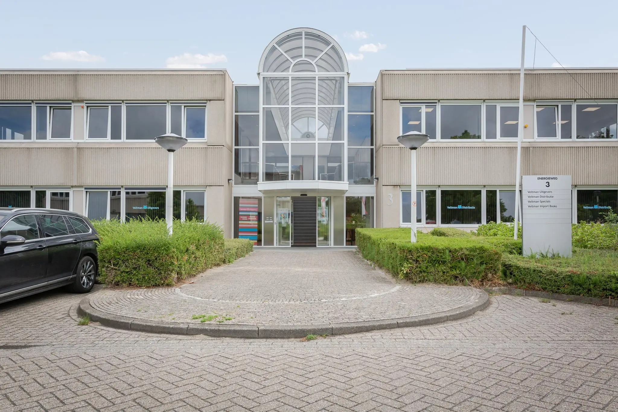 Vooraanzicht van een kantoorgebouw aan de Energieweg 3 met een moderne glazen entree en bedrijfsnaambord op het trottoir.
