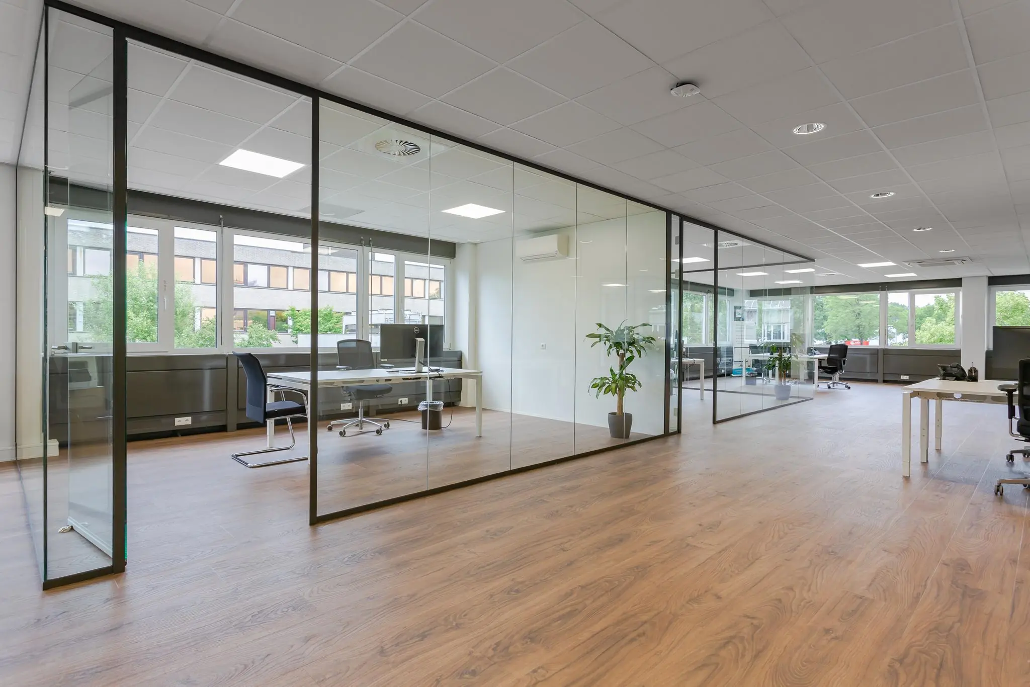Moderne kantoorruimte aan de Energieweg met glazen wanden, houten vloer en werkplekken met bureaus.
