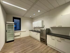 Moderne bedrijfskeuken aan de Zekeringstraat met witte kasten, een vaatwasser en een glazen koelkast.