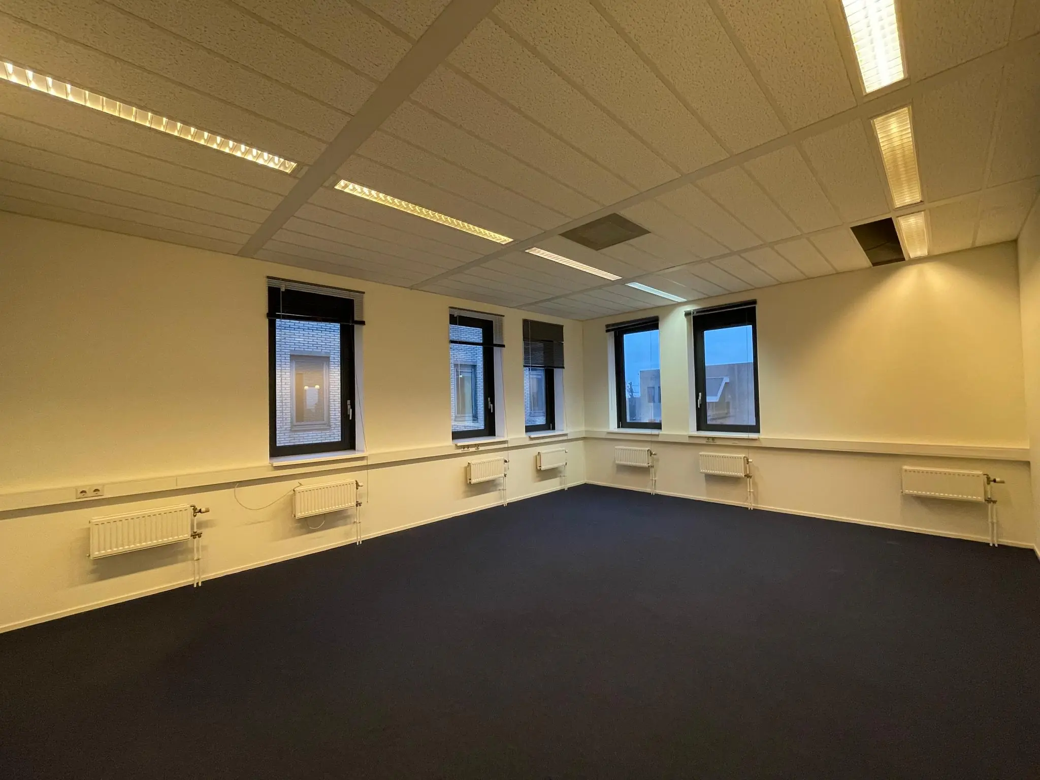 Leeg kantoorpand aan de Zekeringstraat met vier ramen, radiatoren en systeemplafondverlichting.