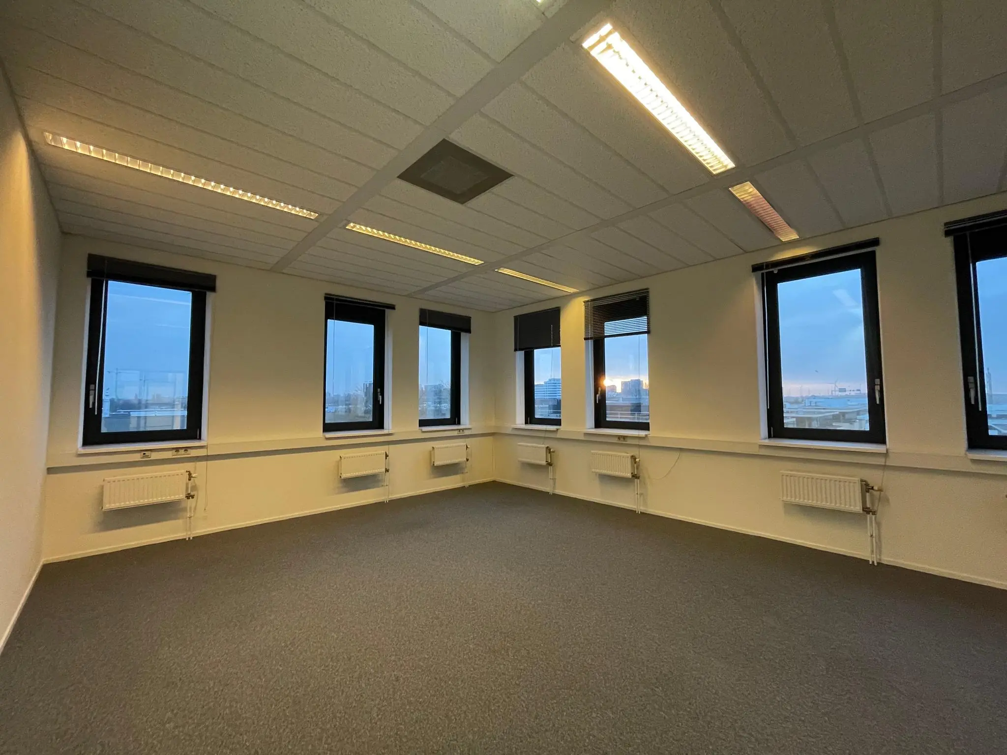 Leeg en licht kantoorruimte met zes grote ramen aan de Zekeringstraat bij zonsondergang.