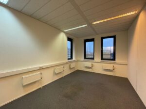 Leeg kantoorkantoor aan de Zekeringstraat met drie ramen, grijze vloerbedekking en witte muren met radiatoren.
