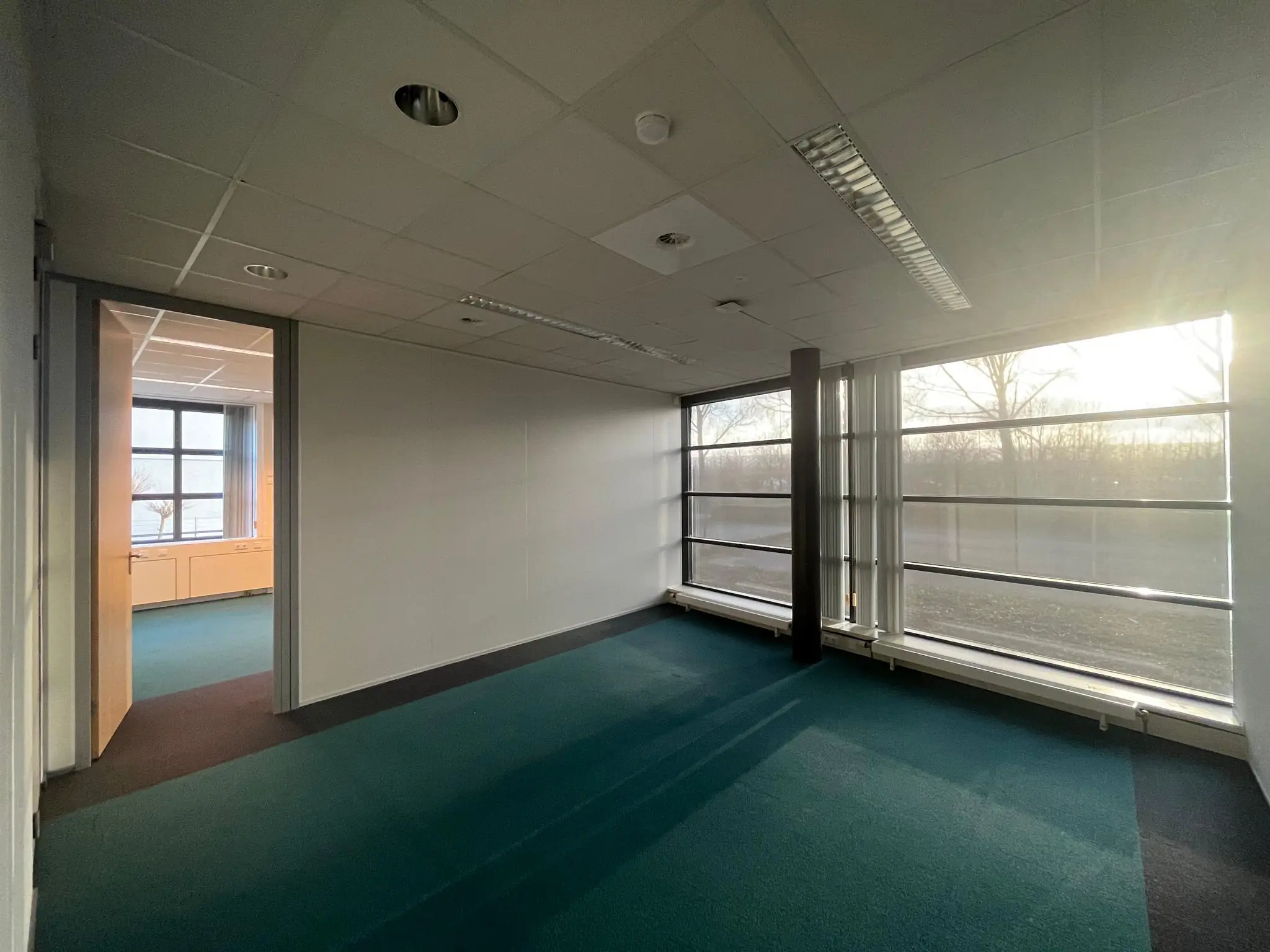 Leeg kantoorruimte met grote ramen aan de Zonnebaan, verlicht door zonlicht.