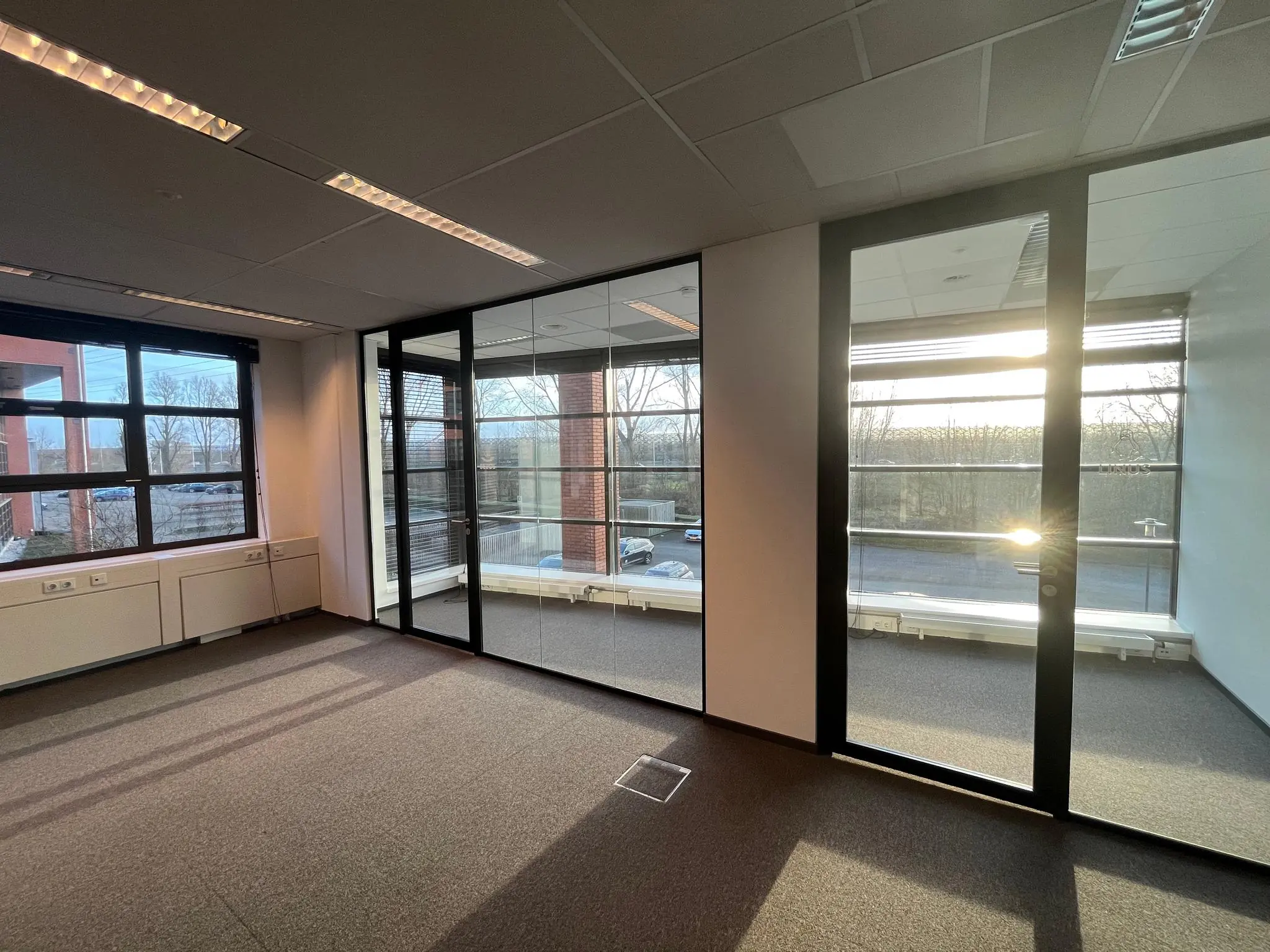 Licht, leeg kantoor aan de Zonnebaan met grote ramen en glazen tussenwand bij zonsondergang.