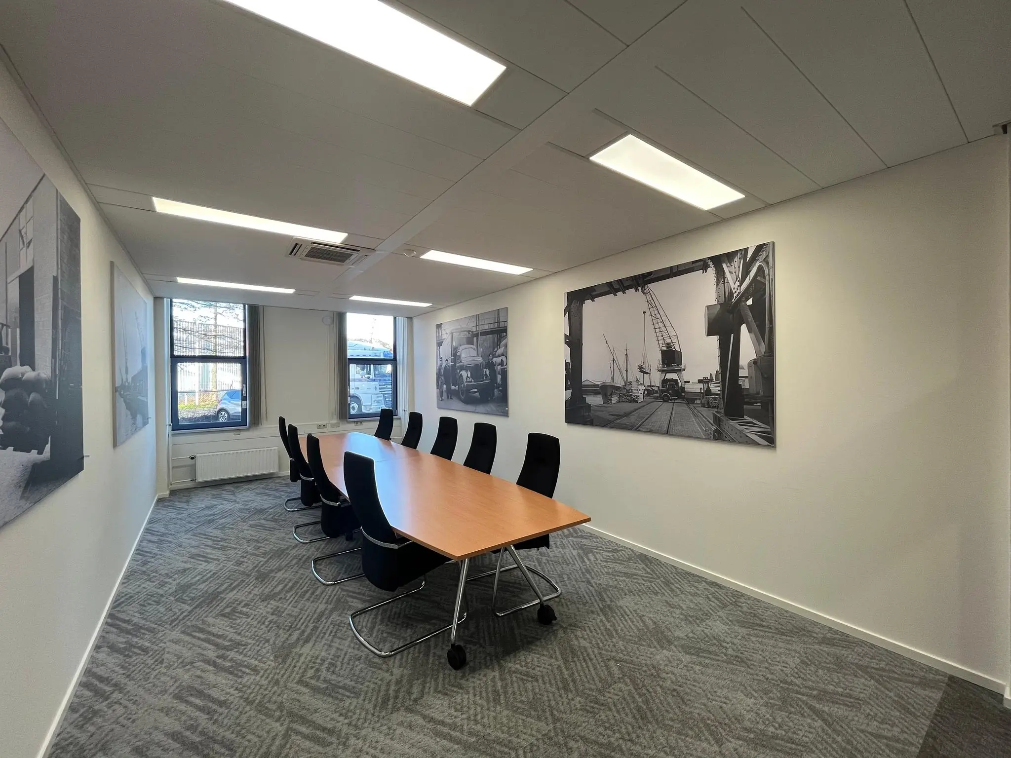 Vergaderruimte met ovale houten tafel, zwarte stoelen en zwart-wit foto's van havenactiviteiten aan de muur in een kantoor aan de Kernkade.
