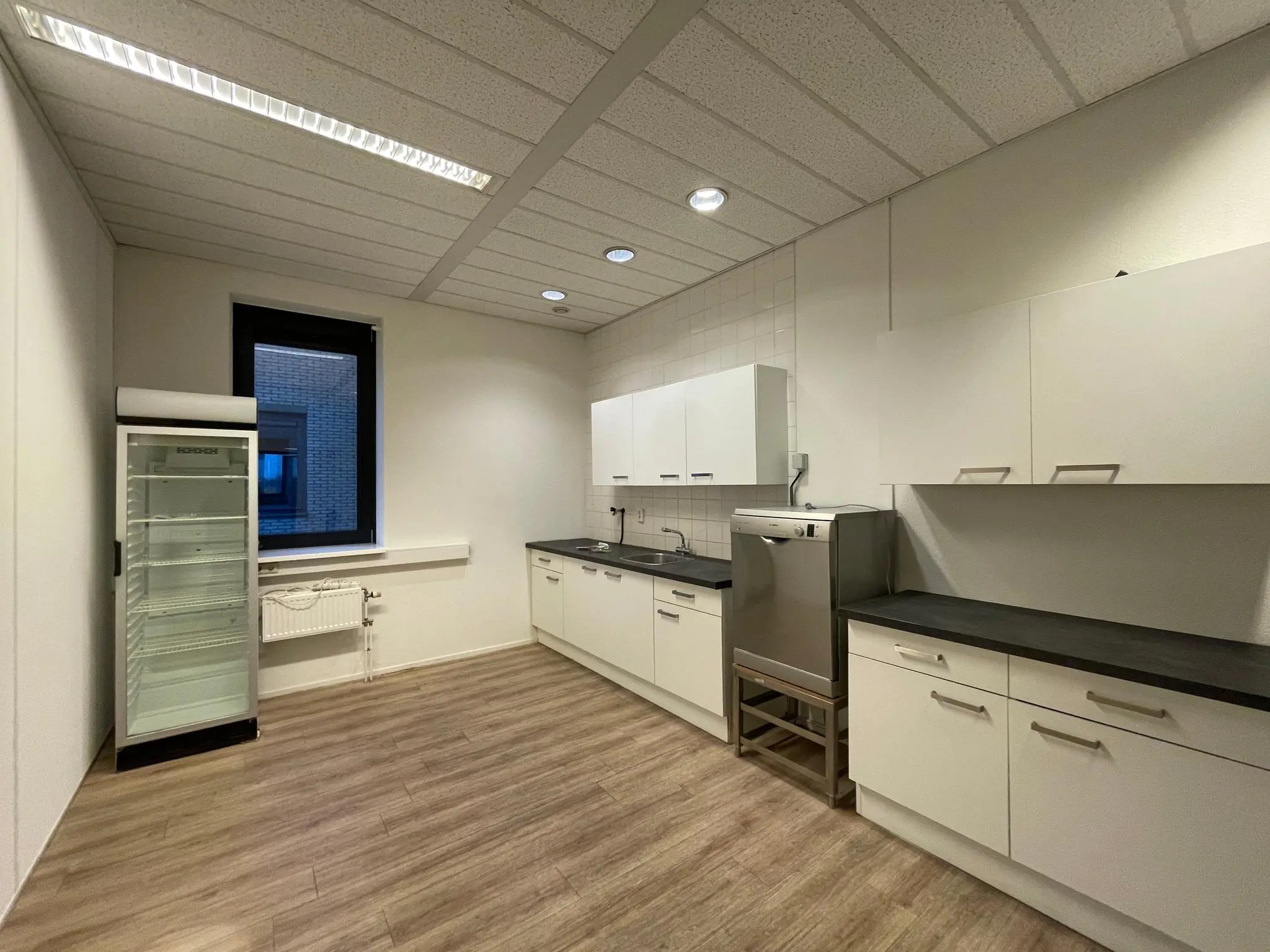 Moderne bedrijfskeuken aan de Zekeringstraat met witte kasten, zwarte werkbladen en een glazen koelkast.