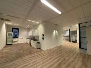 Open kantoorruimte aan de Zekeringstraat met keukenblok, koelkast en glazen kantoordeuren.