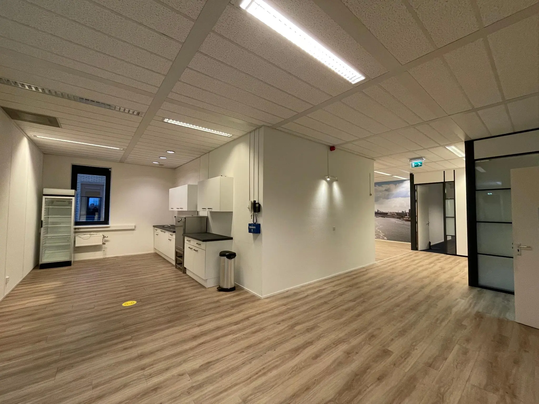 Open kantoorruimte aan de Zekeringstraat met keukenblok, koelkast en glazen kantoordeuren.