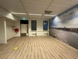 Lege kantoorruimte met houten vloer, een grote fotowand van een rivier met stad en schepen, en een brandslanghaspel aan de muur.