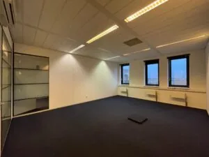 Leeg kantoorruimte in Zekeringstraat met drie ramen, glazen scheidingswand en donker tapijt.