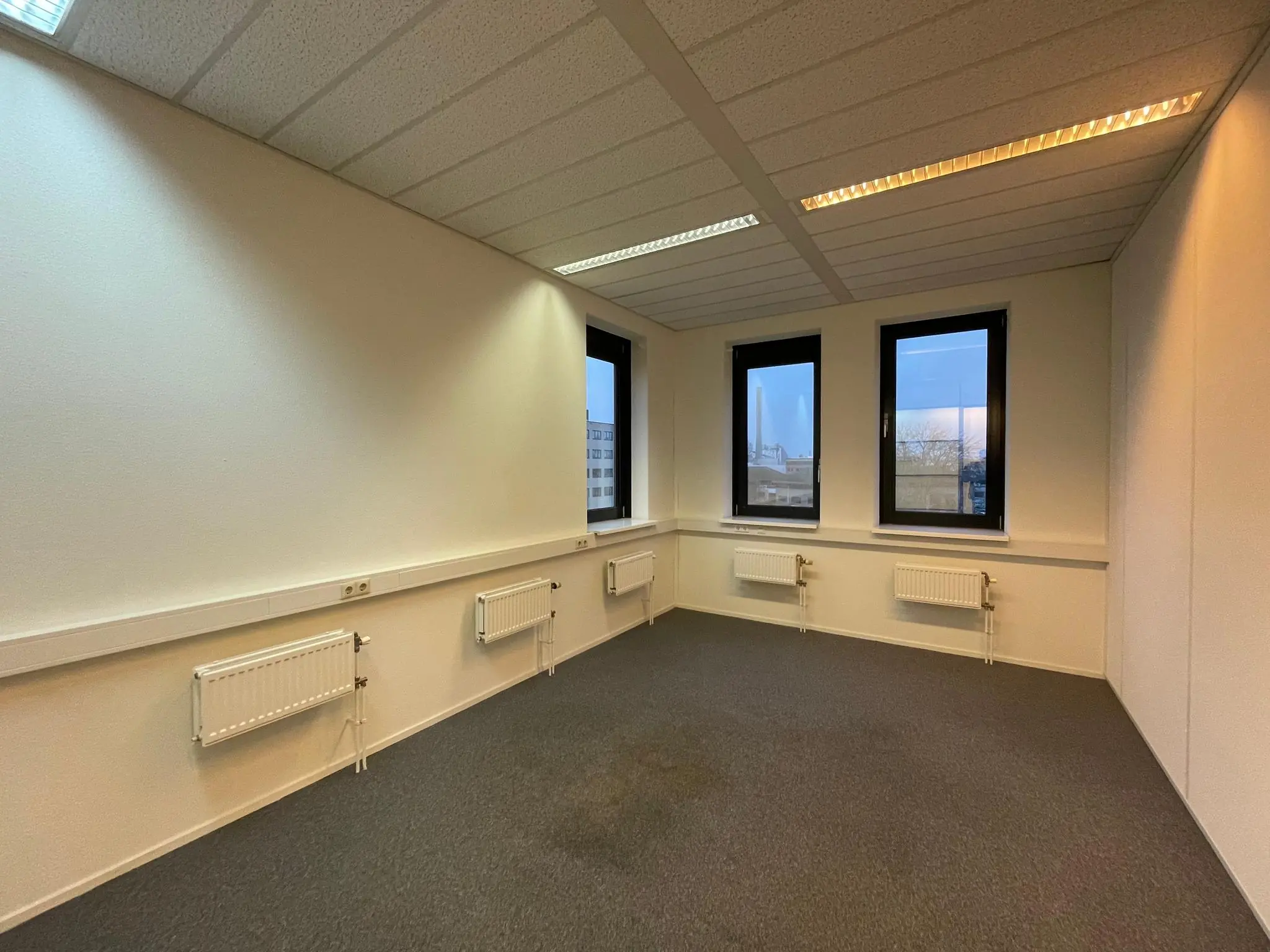 Leege kantoorruimte aan de Zekeringstraat met drie ramen, radiatoren en systeemplafond.