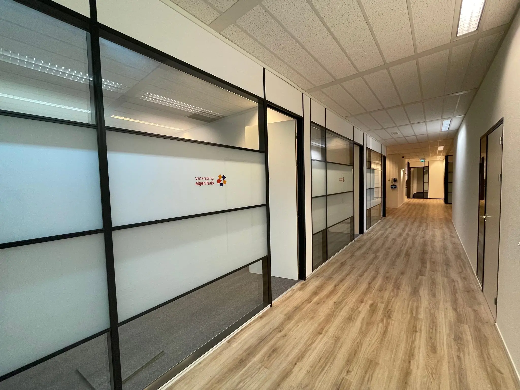 Moderne kantoorhal met glazen kantoorwanden en het logo van Vereniging Eigen Huis op de deur.