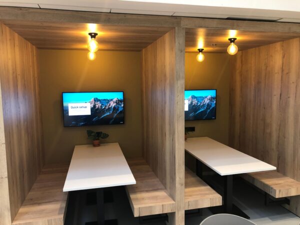 Twee moderne houten werkplekken met ingebouwde tafels, banken, tv-schermen en warme verlichting op Newtonlaan.