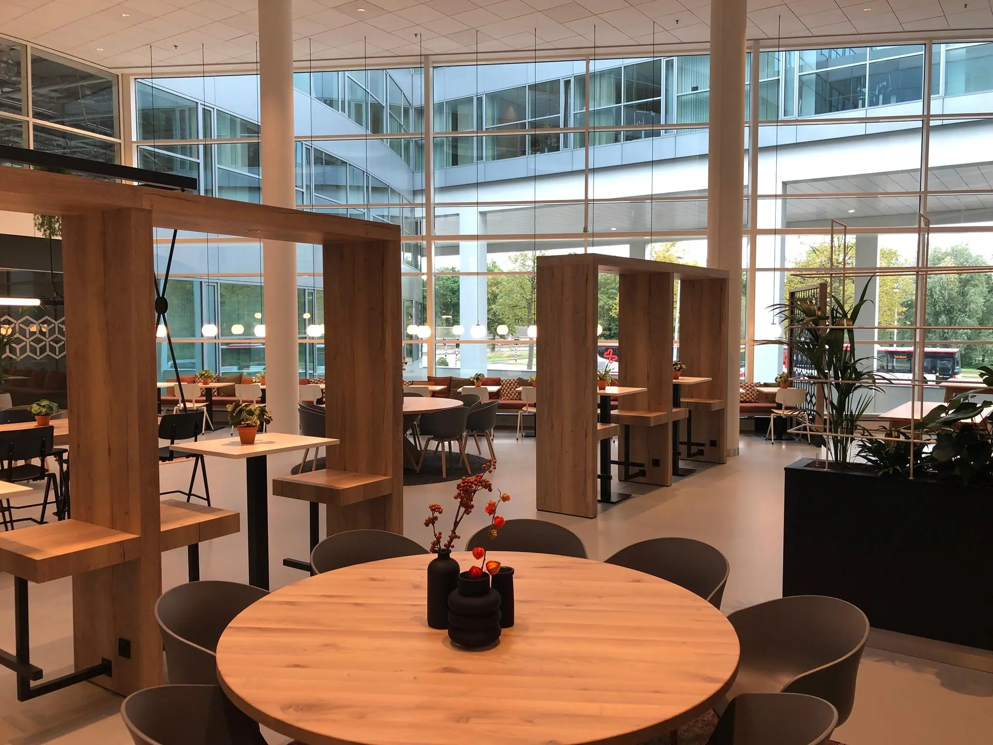 Modern ingerichte bedrijfsrestaurant aan de Newtonlaan met houten zitgedeeltes, ronde tafels en grote glazen ramen.