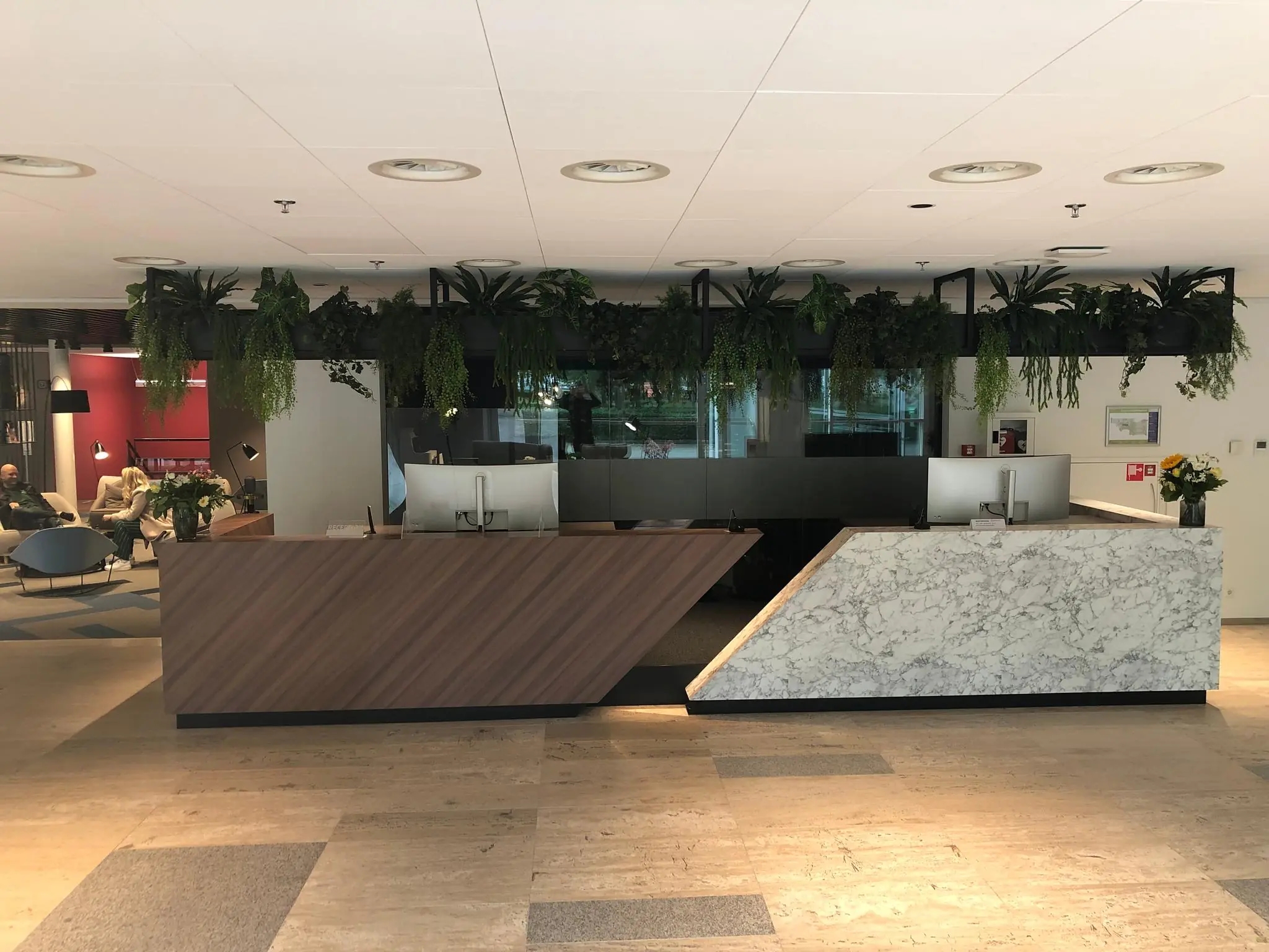 Moderne receptiebalie met hout en marmer in een kantoor aan de Newtonlaan, omringd door hangende planten.
