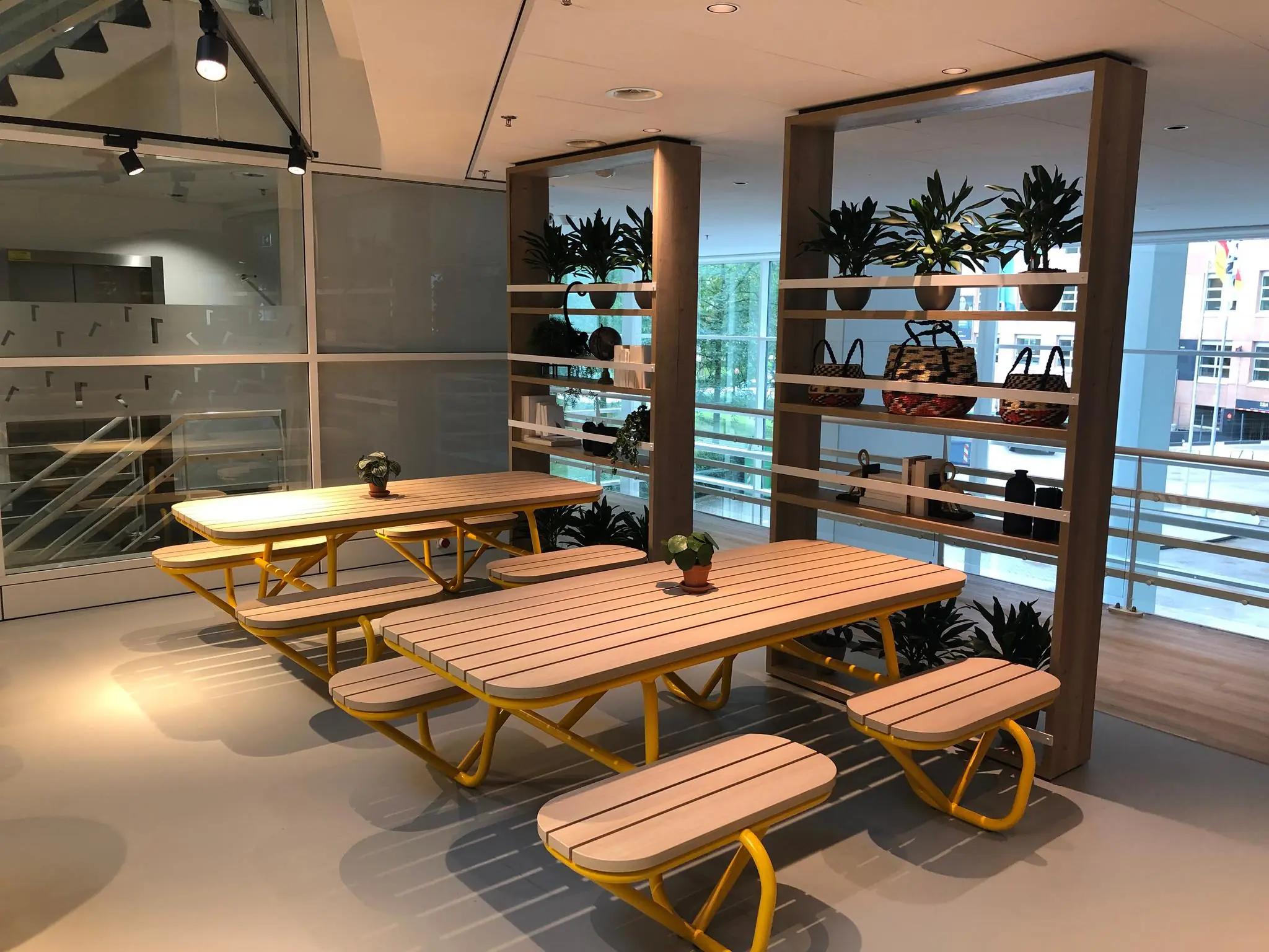 Zitgedeelte met houten picknicktafels en gele poten in een modern kantoorpand aan de Newtonlaan.