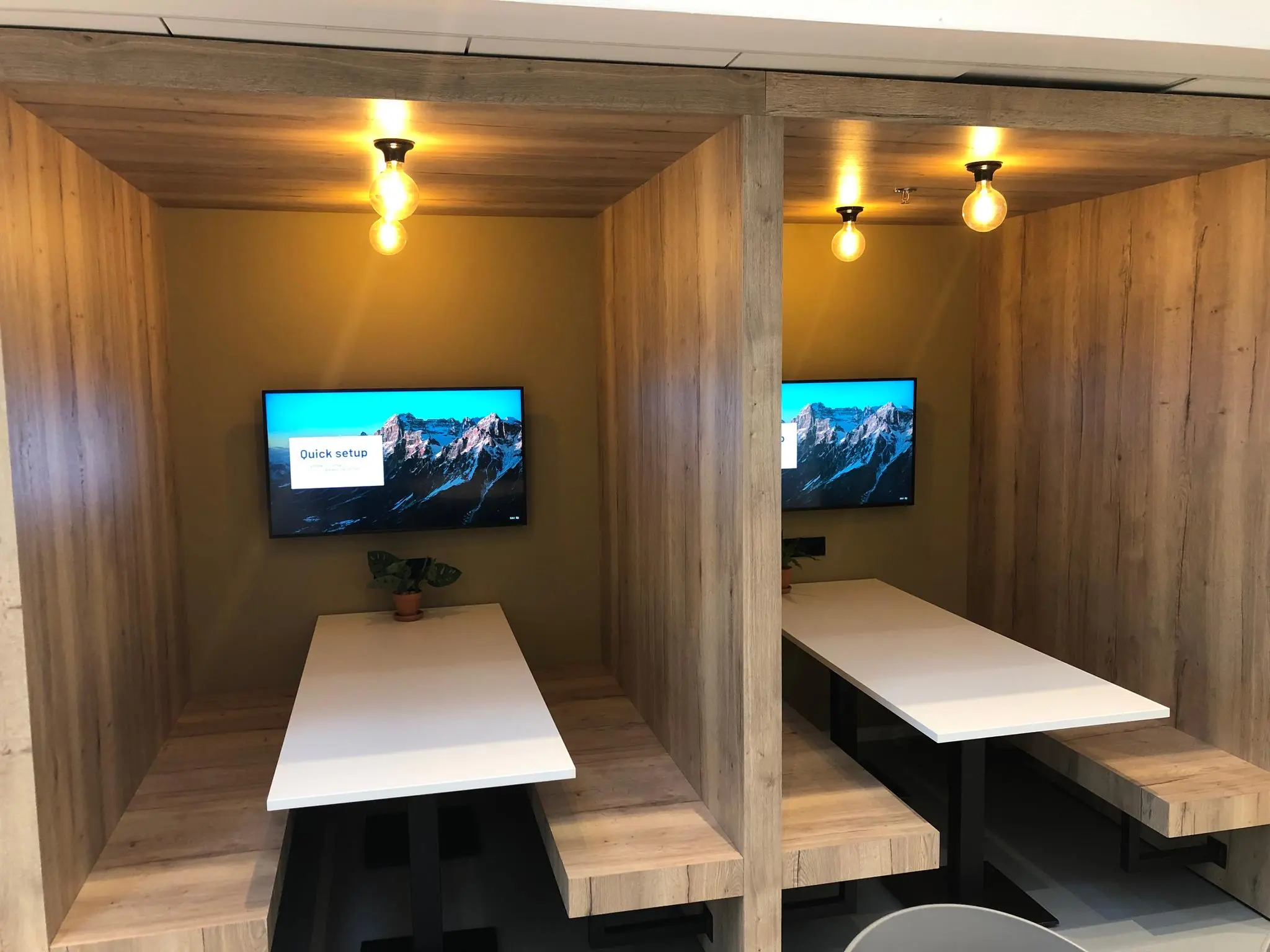 Twee moderne werk- of vergadernissen met houten wanden, witte tafels, muurmonitors en sfeerverlichting in een kantoor aan de Newtonlaan.