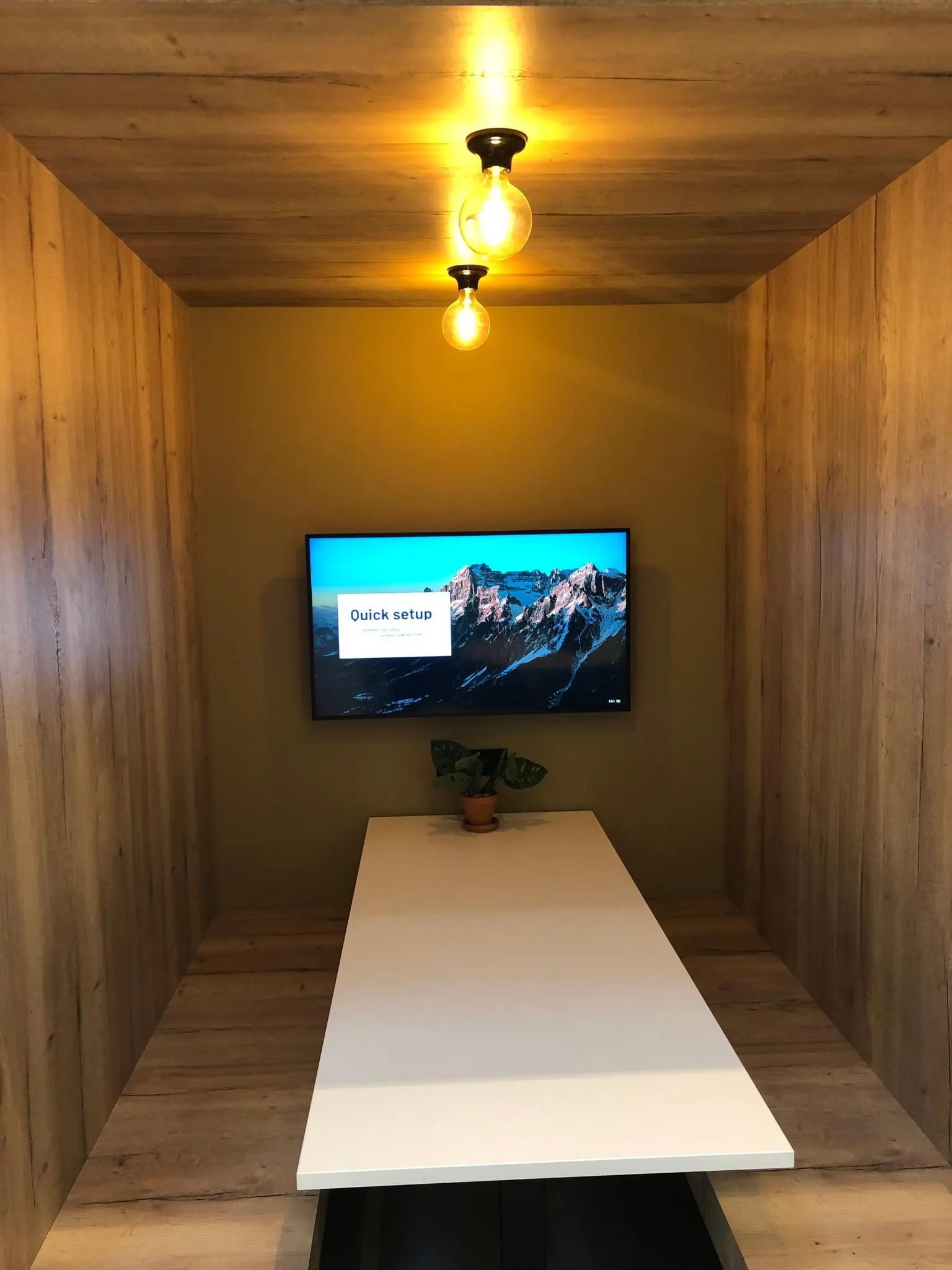 Moderne vergaderruimte met houten wanden, een witte tafel, een beeldscherm aan de muur en warme verlichting aan het plafond.