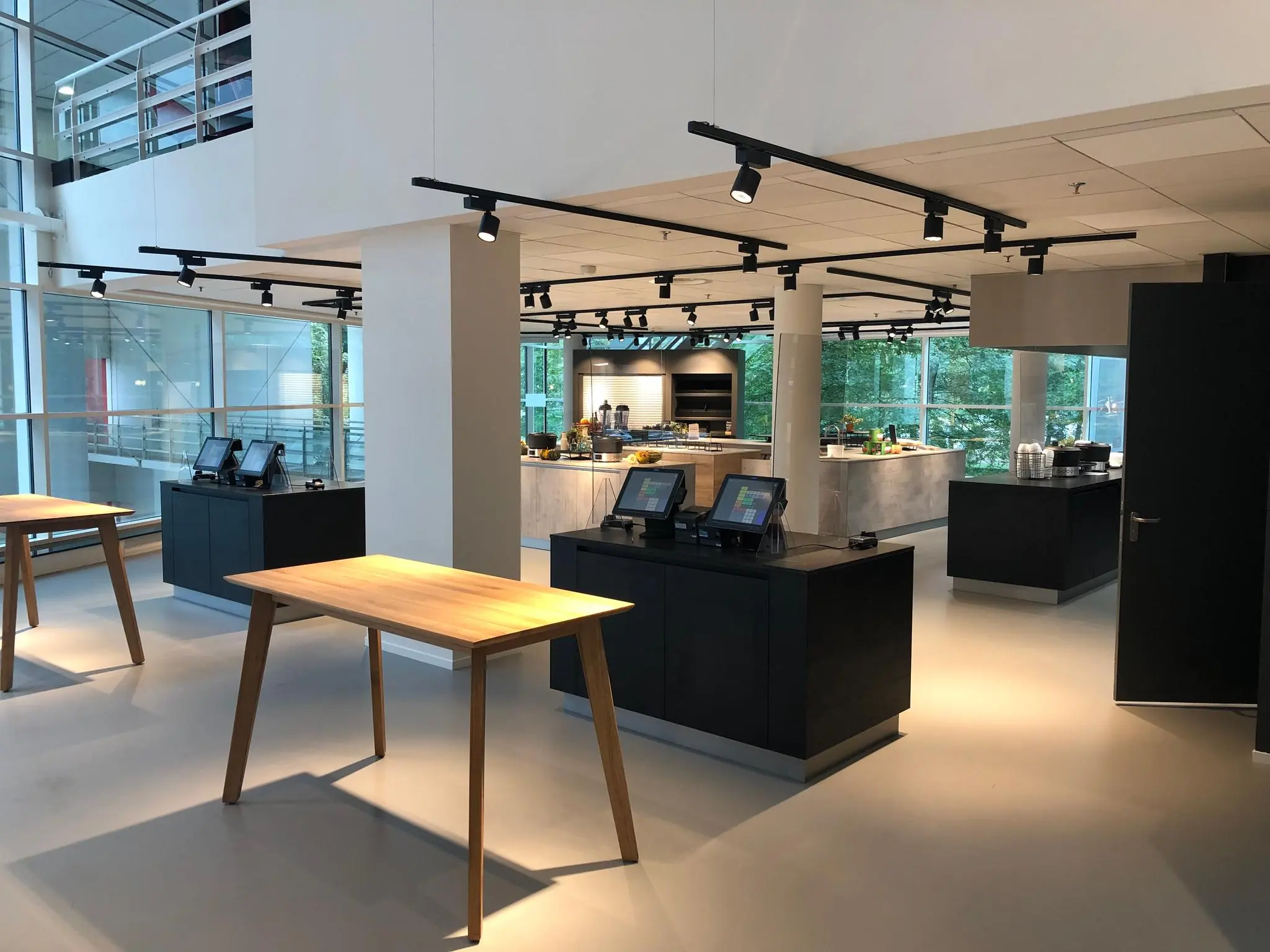 Moderne en open bedrijfsrestaurant op Newtonlaan met zelfbedieningsstations en houten tafels.