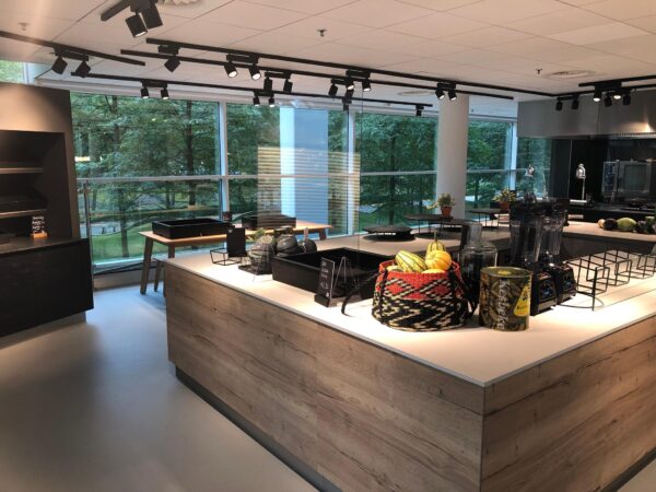 Moderne, ruim opgezette bedrijfskeuken aan de Newtonlaan met grote ramen, blenders en een mand met decoratieve kalebassen op het aanrecht.