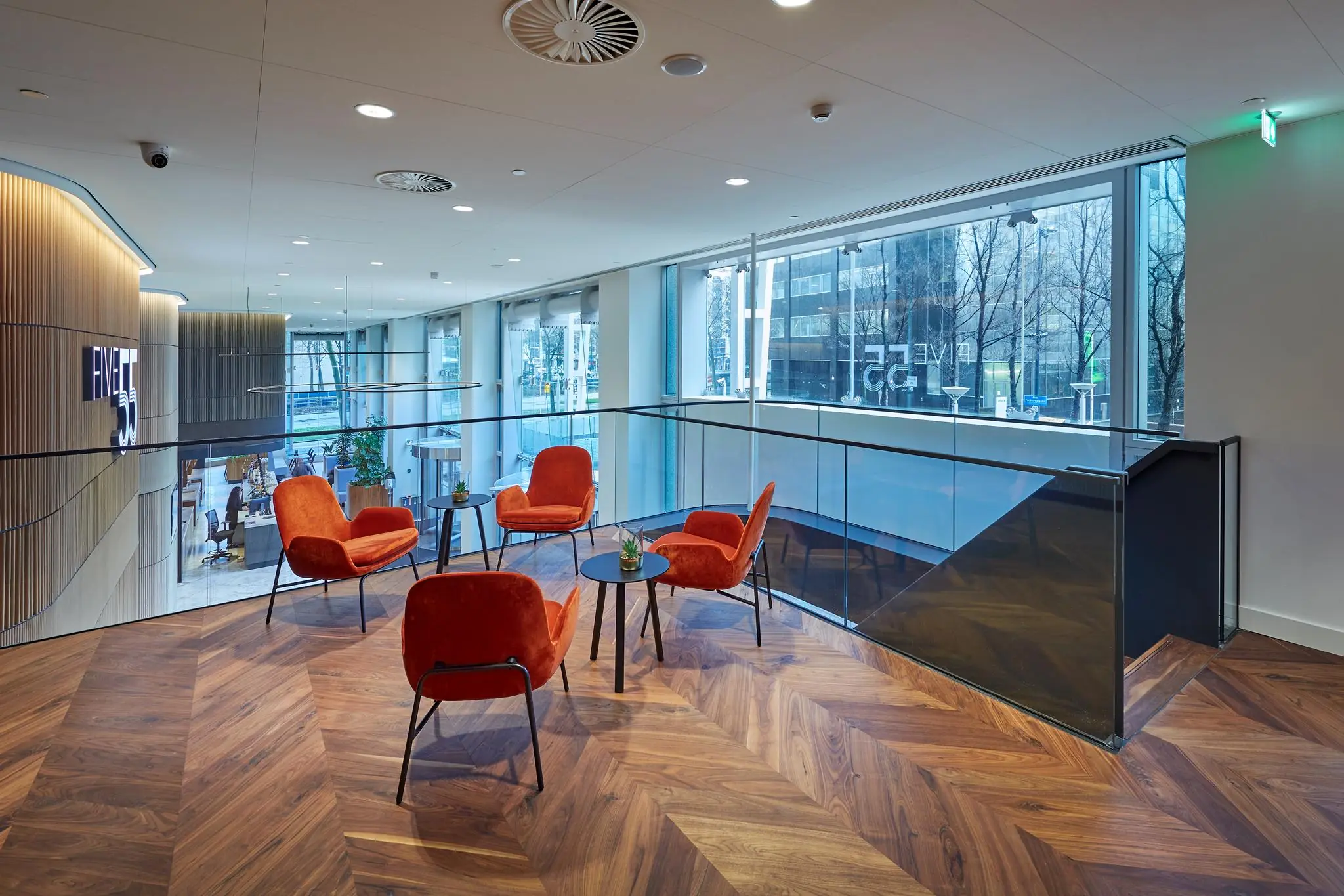 Moderne zithoek met oranje stoelen en houten vloer in het kantoorpand FIVE55 aan de Blaak in Rotterdam.