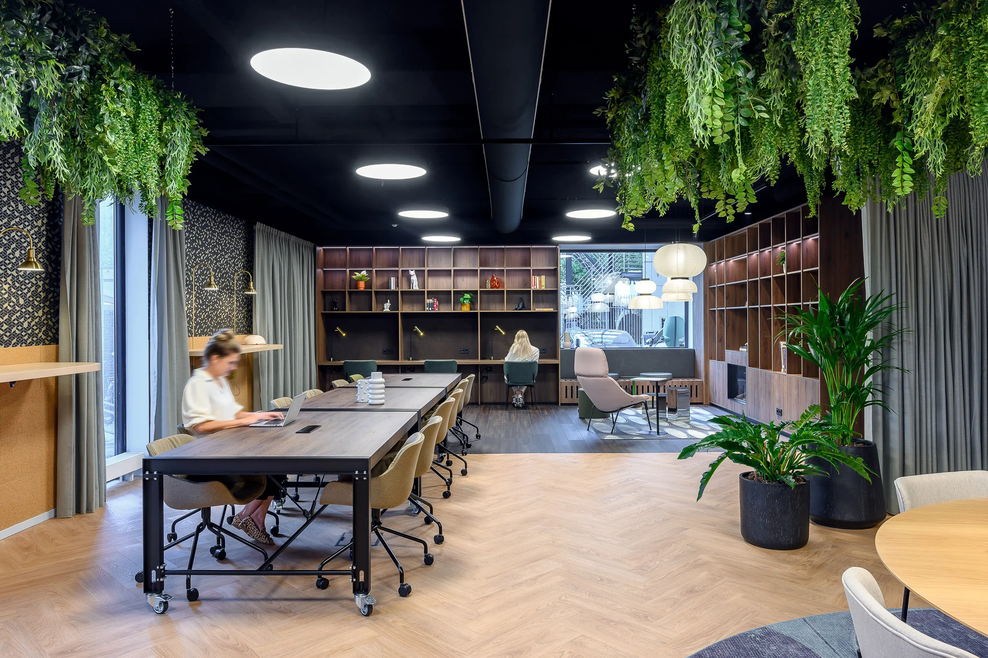 Stijlvolle en moderne kantoorruimte met houten vloeren, hangplanten, werkplekken en loungehoek.