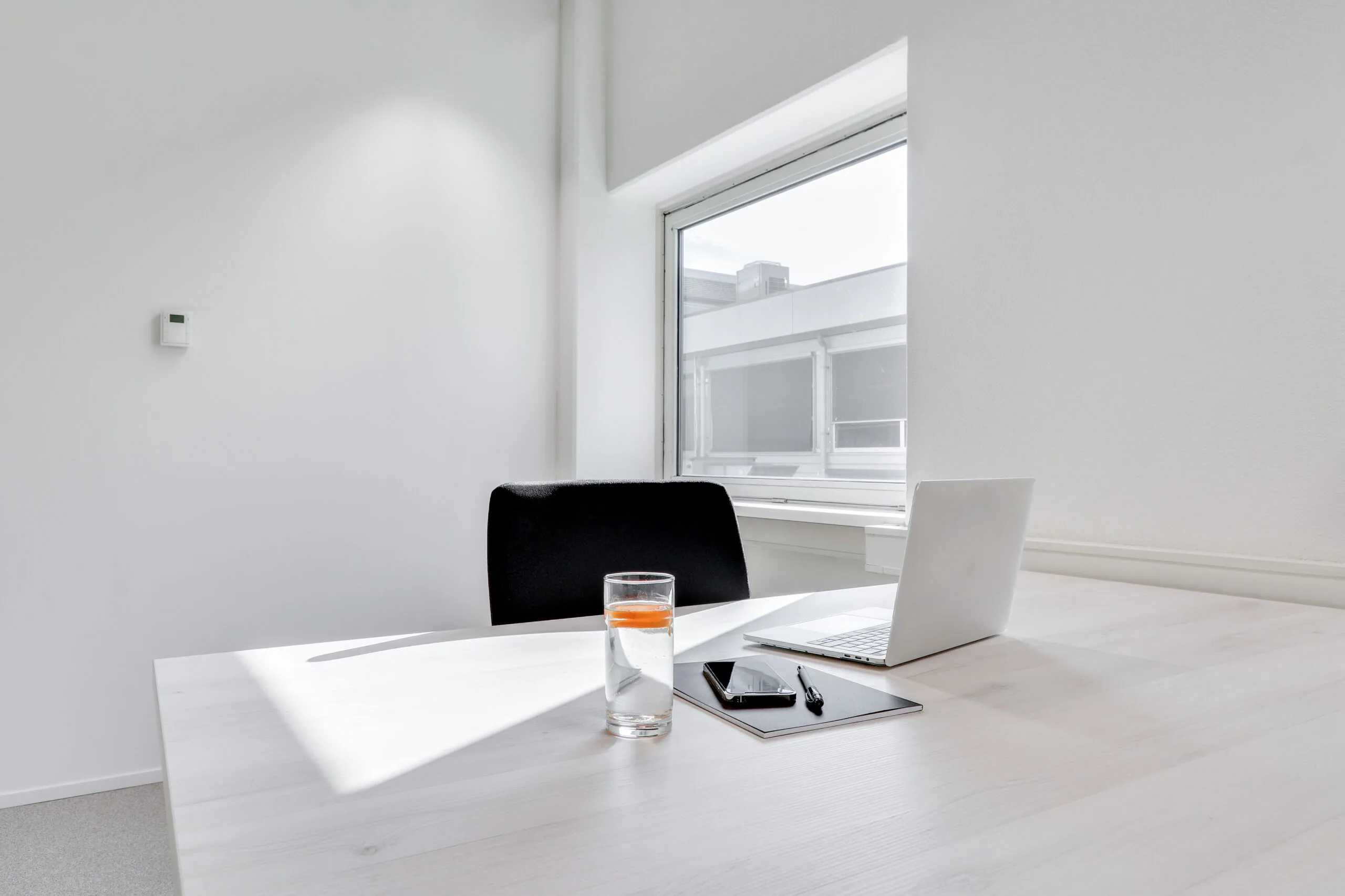 Minimalistisch ingericht bureau bij Amsterdam Schinkel-Workspace met laptop, notitieboek, pen, smartphone en een glas water met sinaasappel.