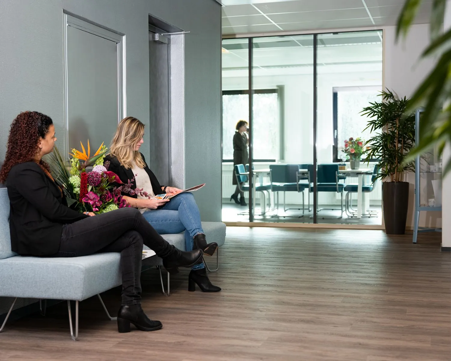 Twee vrouwen zitten in een wachtruimte van kantoorruimte aan de Bolderweg 2a in Almere, met op de achtergrond een vergaderruimte.