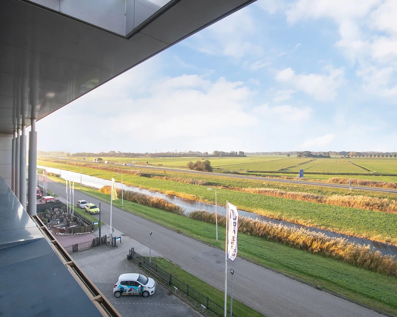 Uitzicht vanaf een kantoorruimte aan de Carlsonstraat 13 in Kampen over een landelijke weg, kanaal en uitgestrekte weilanden.