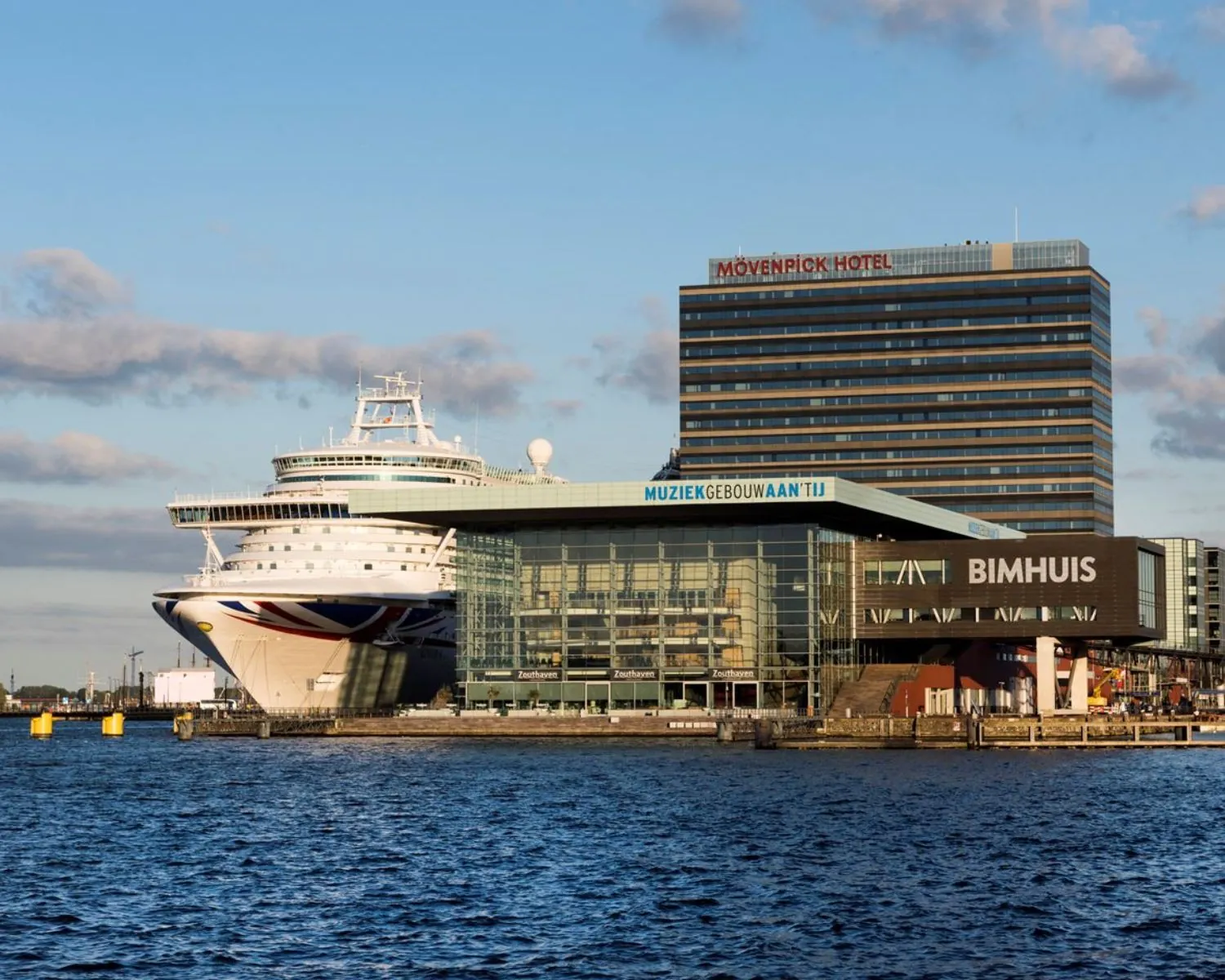 Uitzicht op het Muziekgebouw aan ’t IJ, het Bimhuis en het Movenpick Hotel in Amsterdam met een aangemeerd cruiseschip.