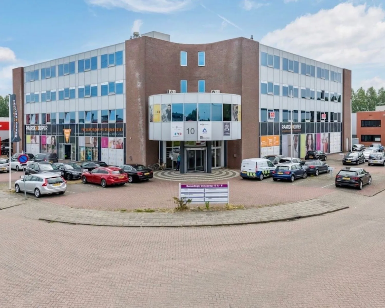 Voorgevel van een modern kantoorpand aan de Kamerlingh Onnesweg 10 in Barendrecht met parkeerterrein en geparkeerde auto's.