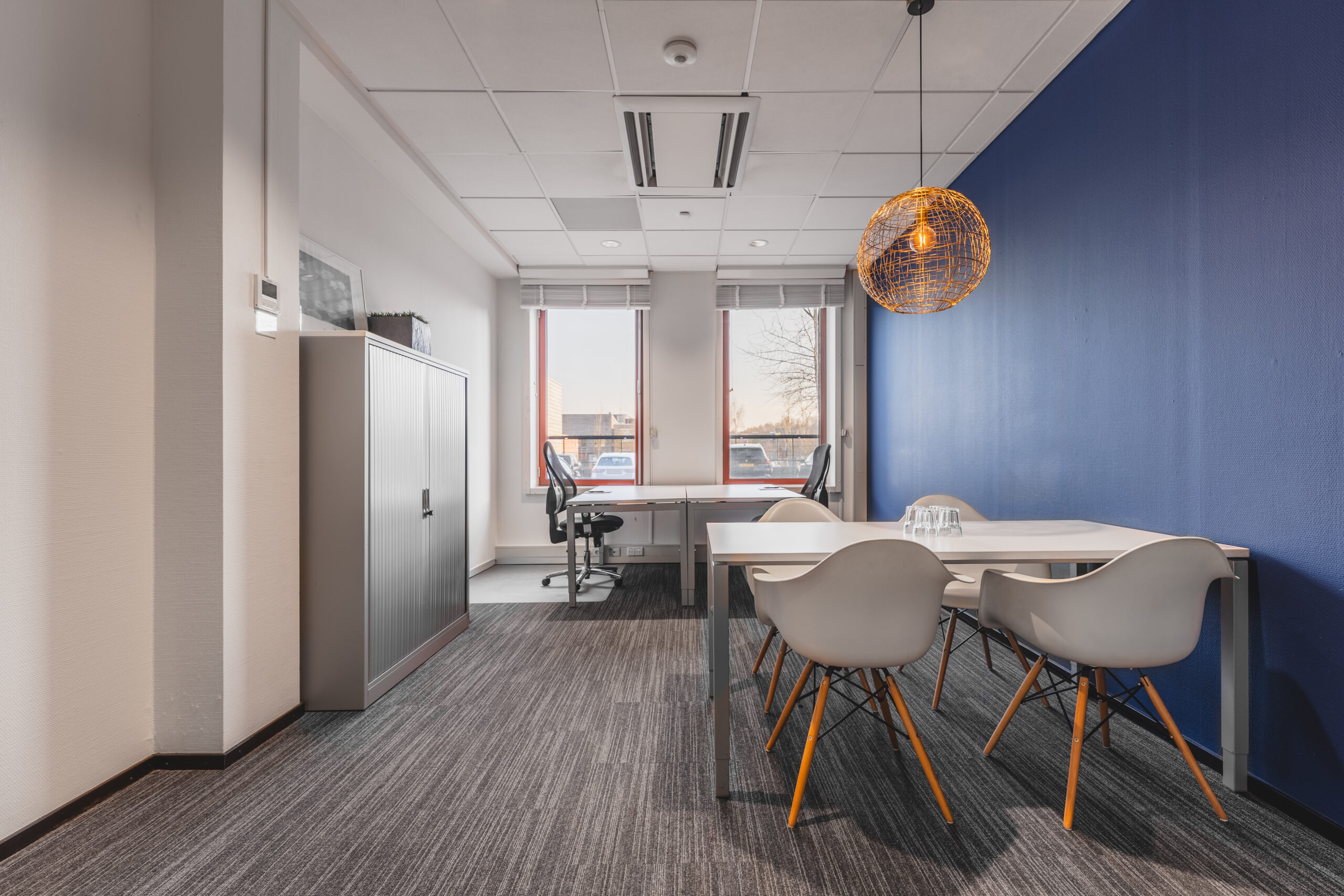 Een modern kantoor met een blauwe muur, bureaustoelen en een vergadertafel met stoelen.
