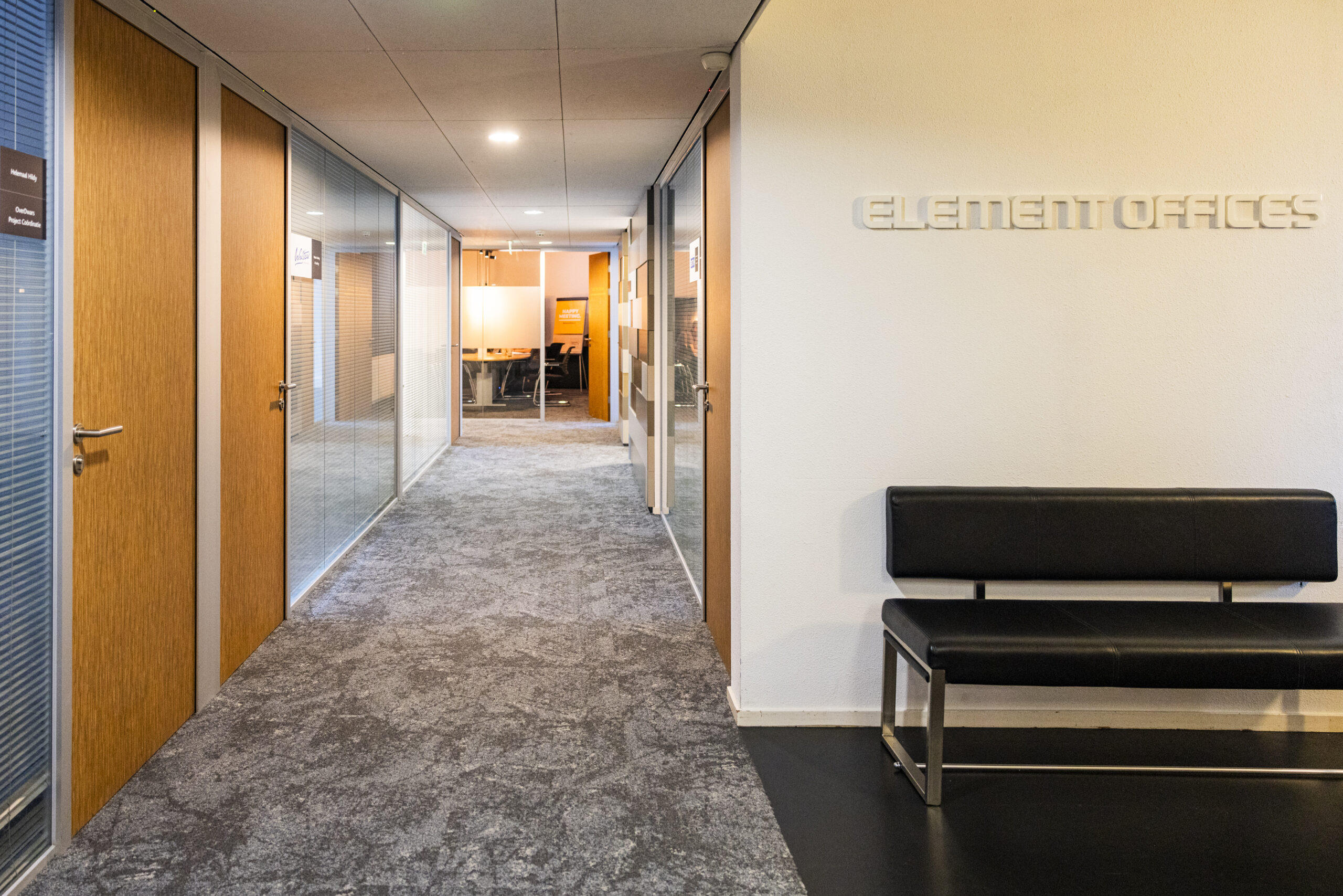Een moderne kantoorhal met glazen wanden en een zwarte bank, met het bord "ELEMENT OFFICES" aan de muur.