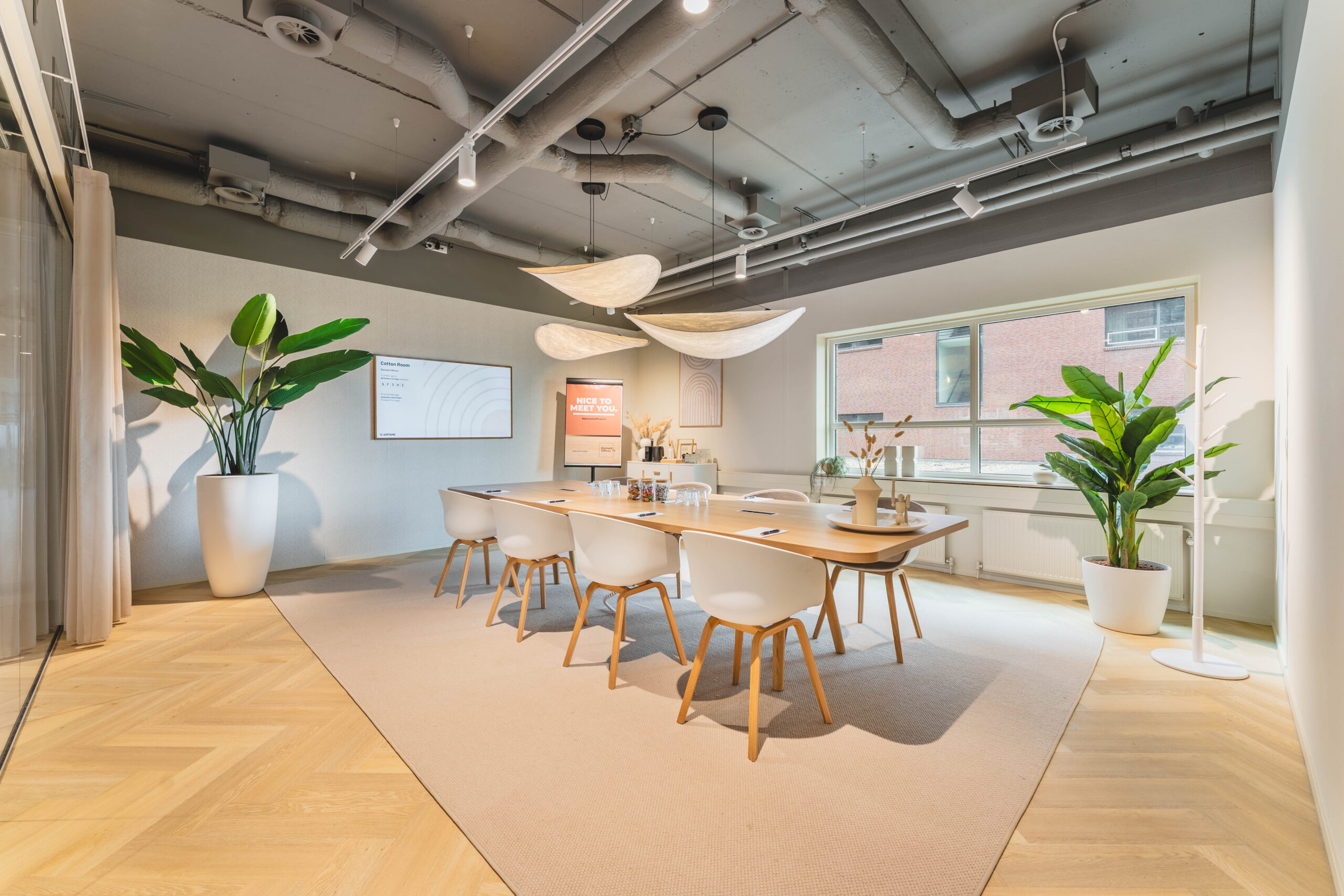 Een moderne vergaderruimte met een grote houten tafel, witte stoelen en planten in potten.