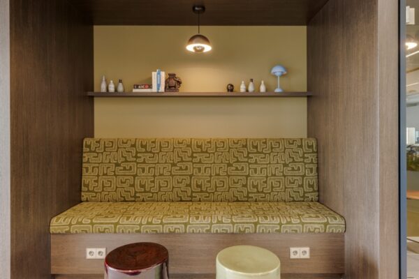 Een moderne zitplek met een groene bank en decoratieve voorwerpen op een plank erboven.